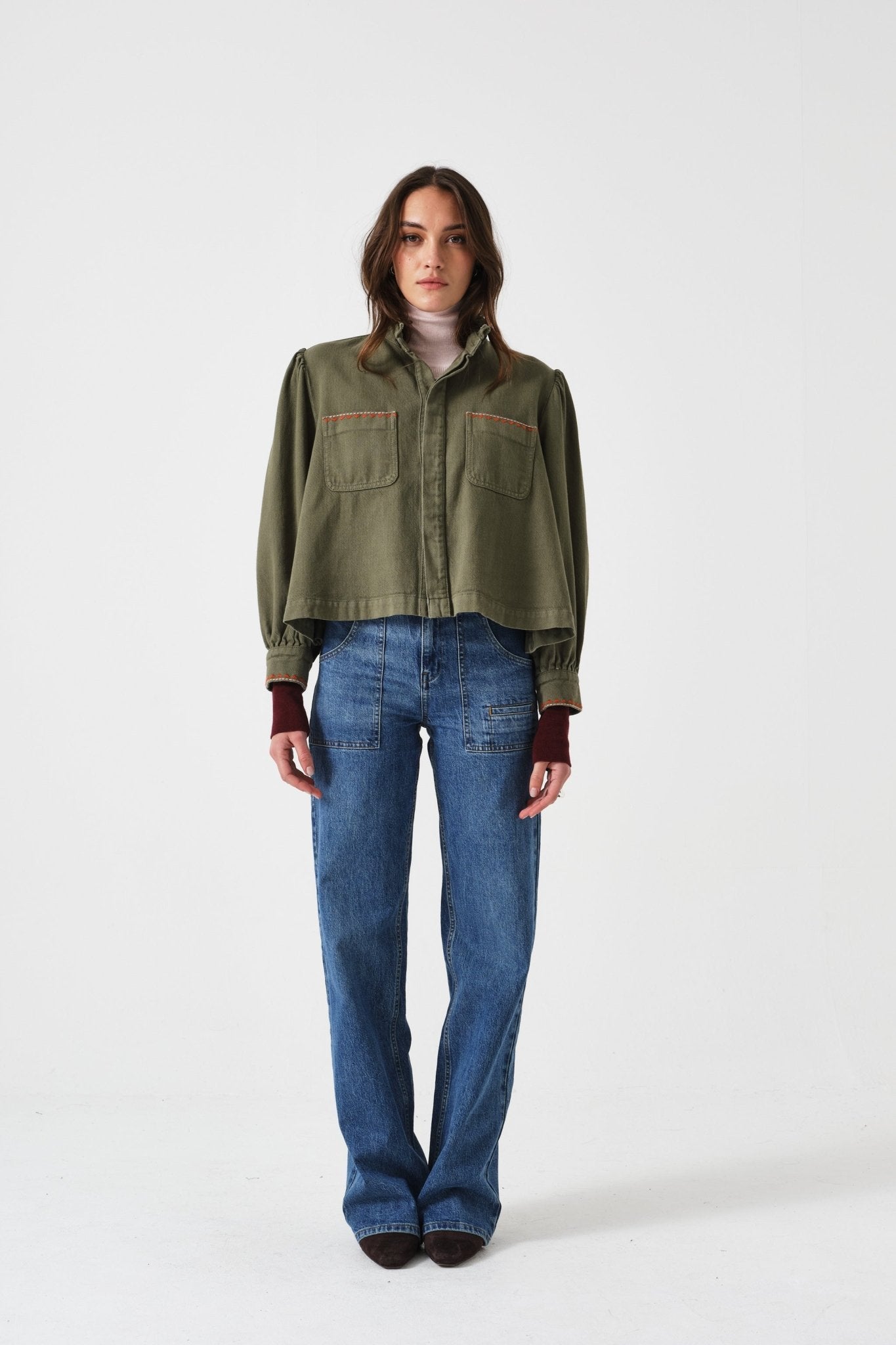 Woman wearing a olive green denim jacket with buttons done up, and blue jeans