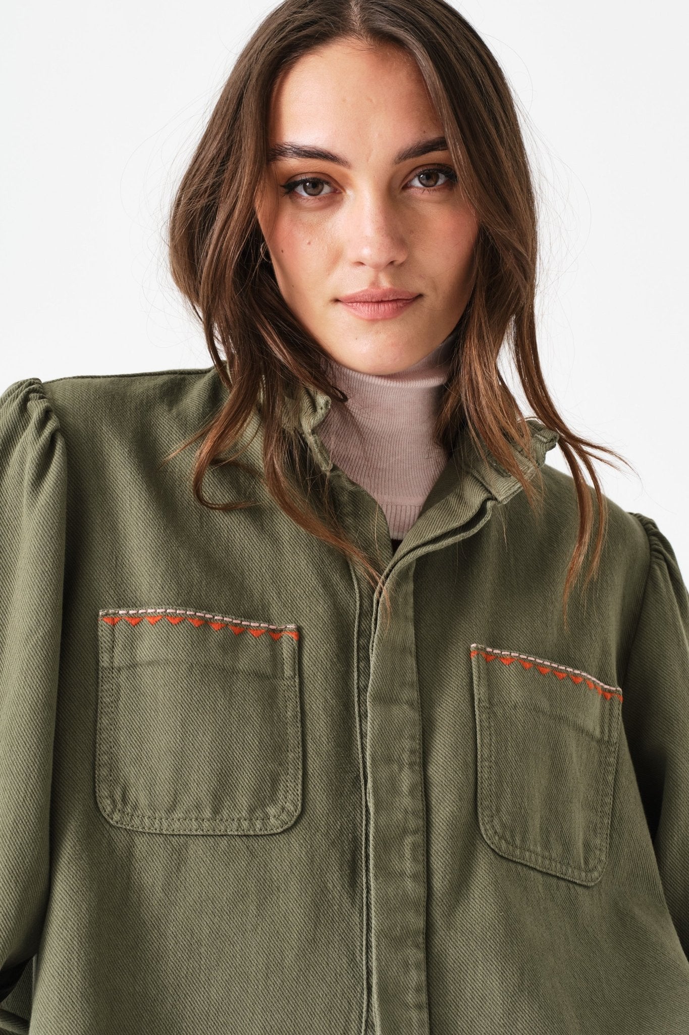 Woman wearing a green jacket with two front pockets and buttons done up 