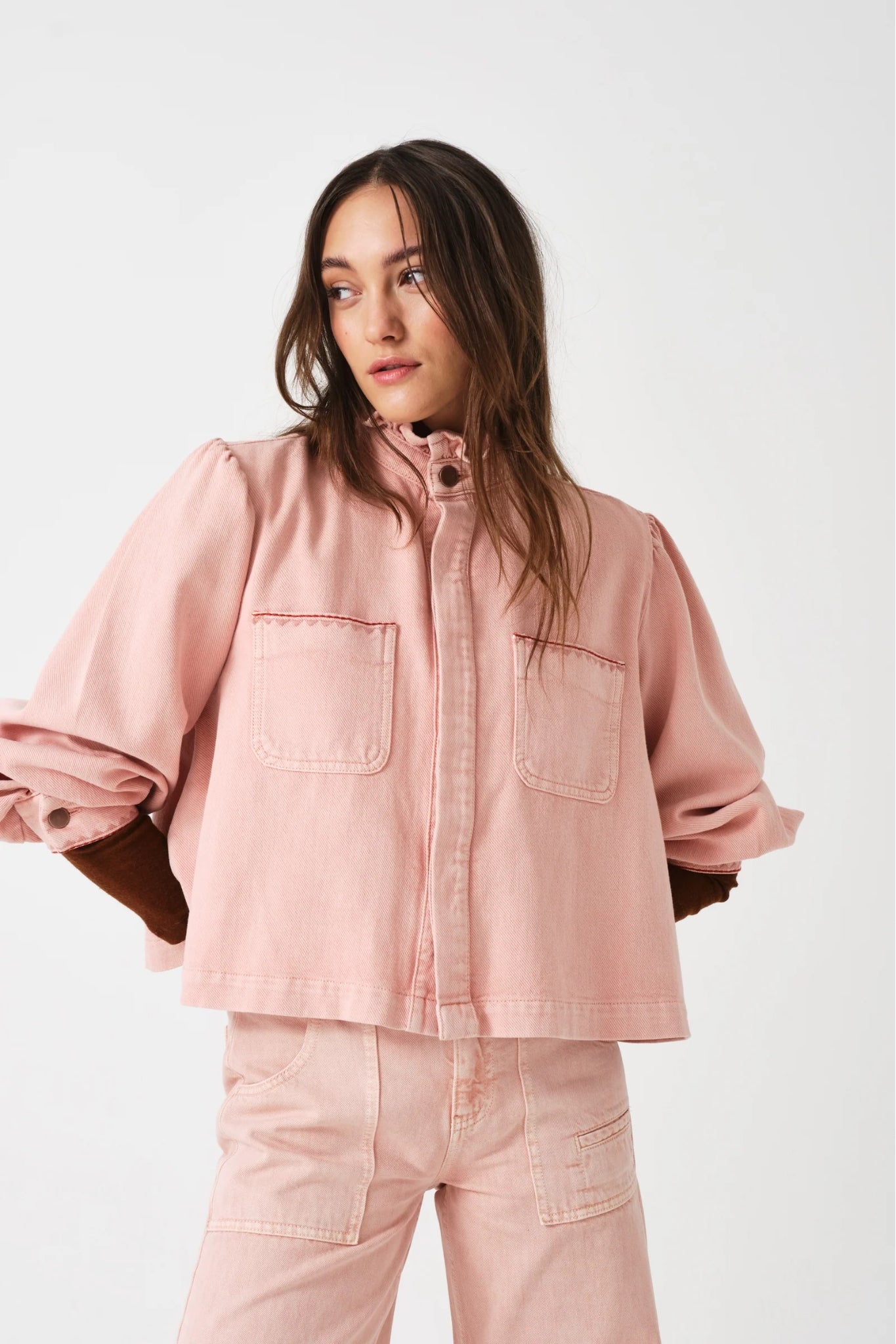 Woman wearing a pink jacket and jeans with arms behind back