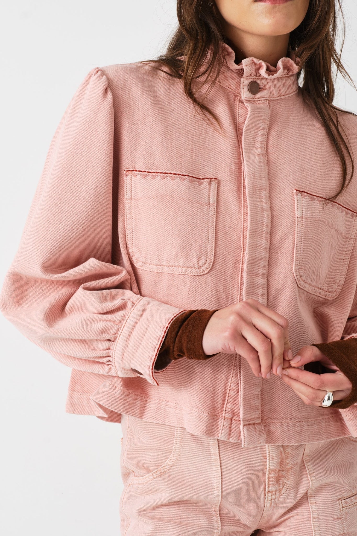 Woman wearing a pink jacket with pockets, ruffled collar buttoned up
