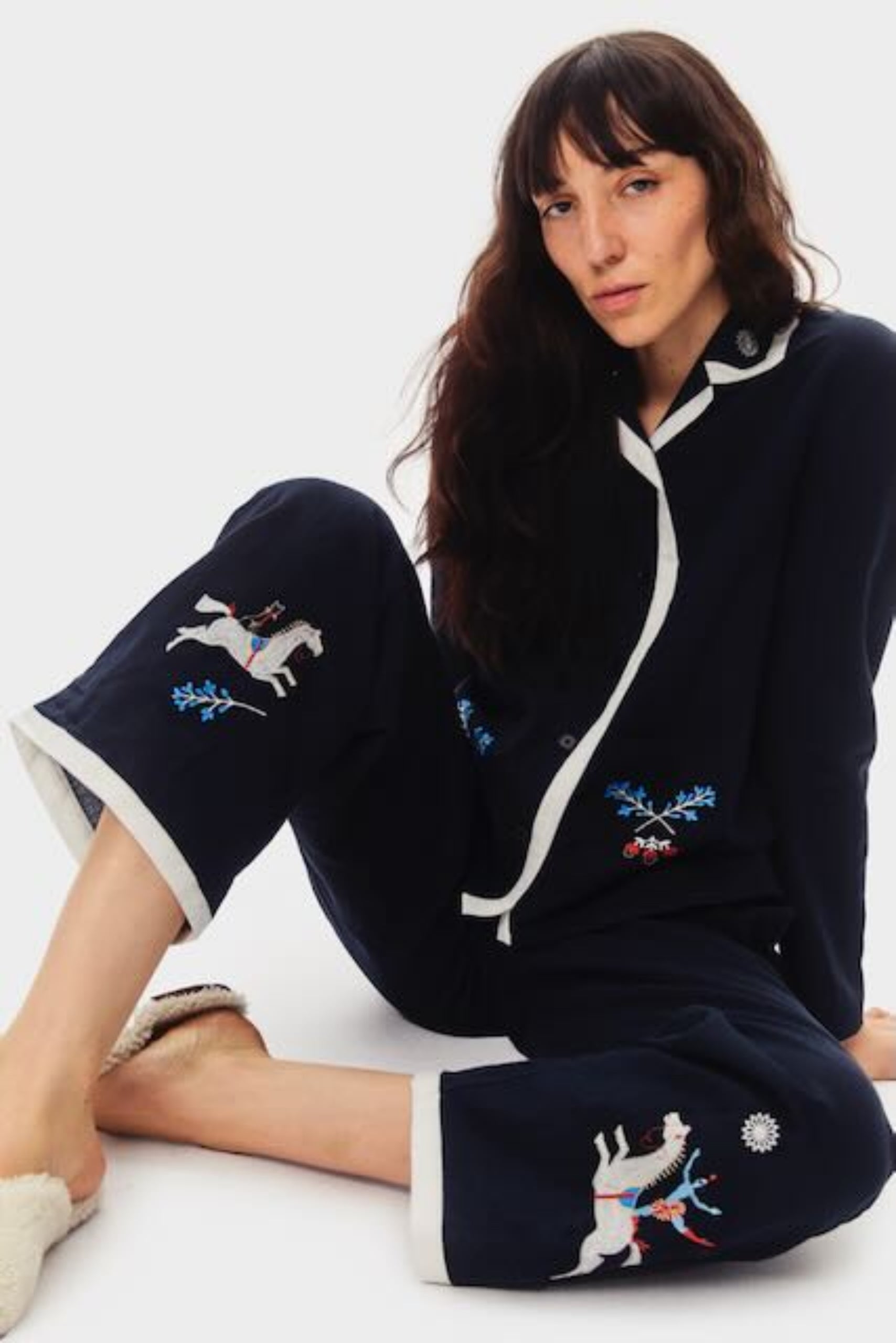 Woman sitting down on floor wearing navy long sleeve cotton - poplin shirt with collar and button front and long pants with embroidery.