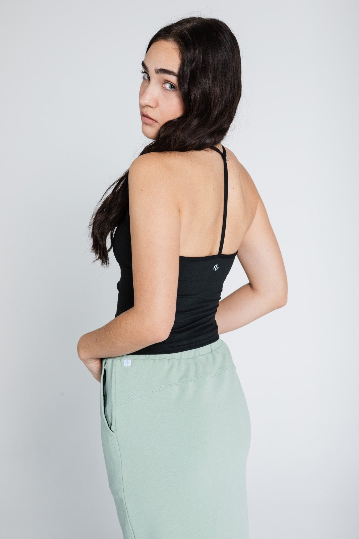 Back of a woman wearing a black sleeveless workout top and green skirt.