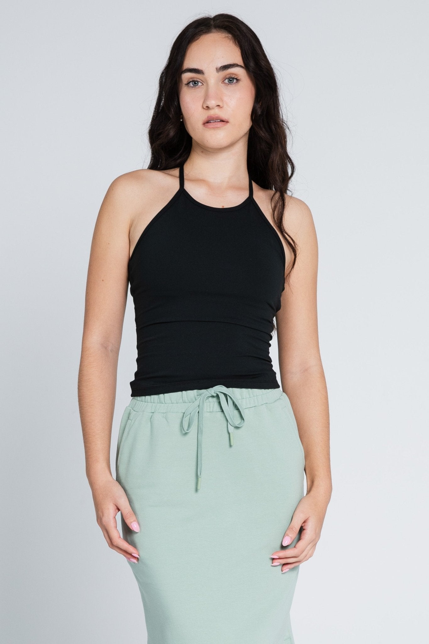 Woman wearing a black sleeveless workout top and green skirt.