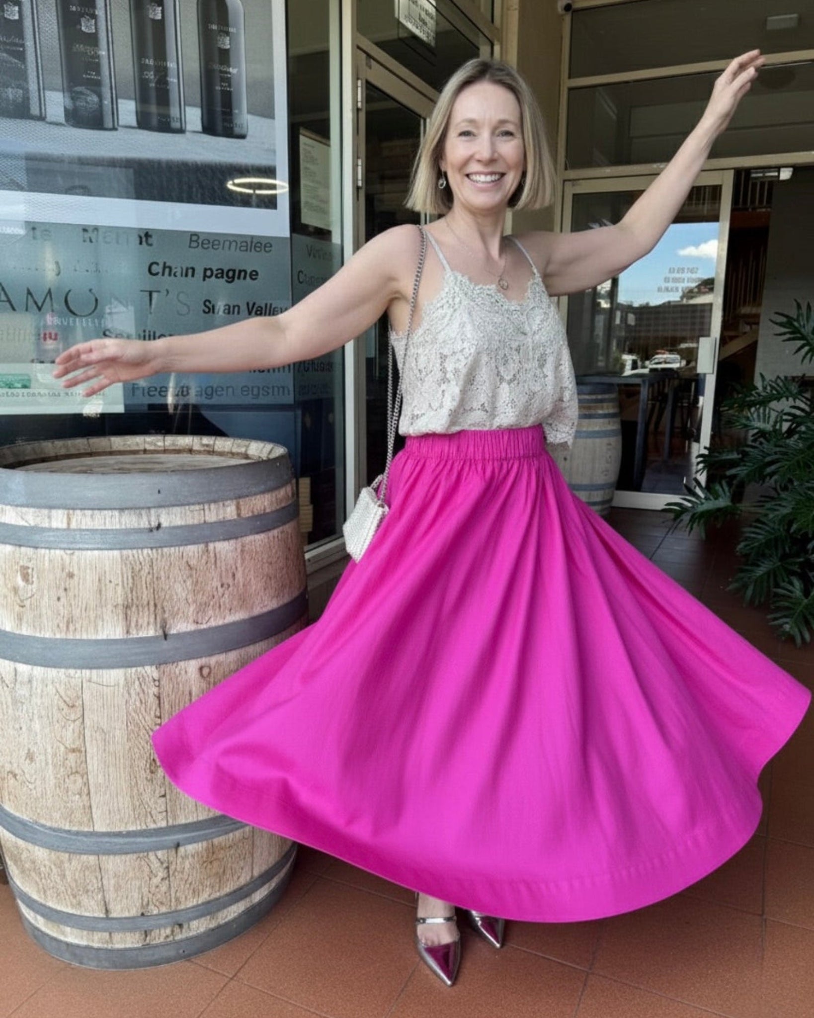Woman in a beige lace top and hot pink elastic waist skirt twirling in front of a barrel at a restaurant entrance.