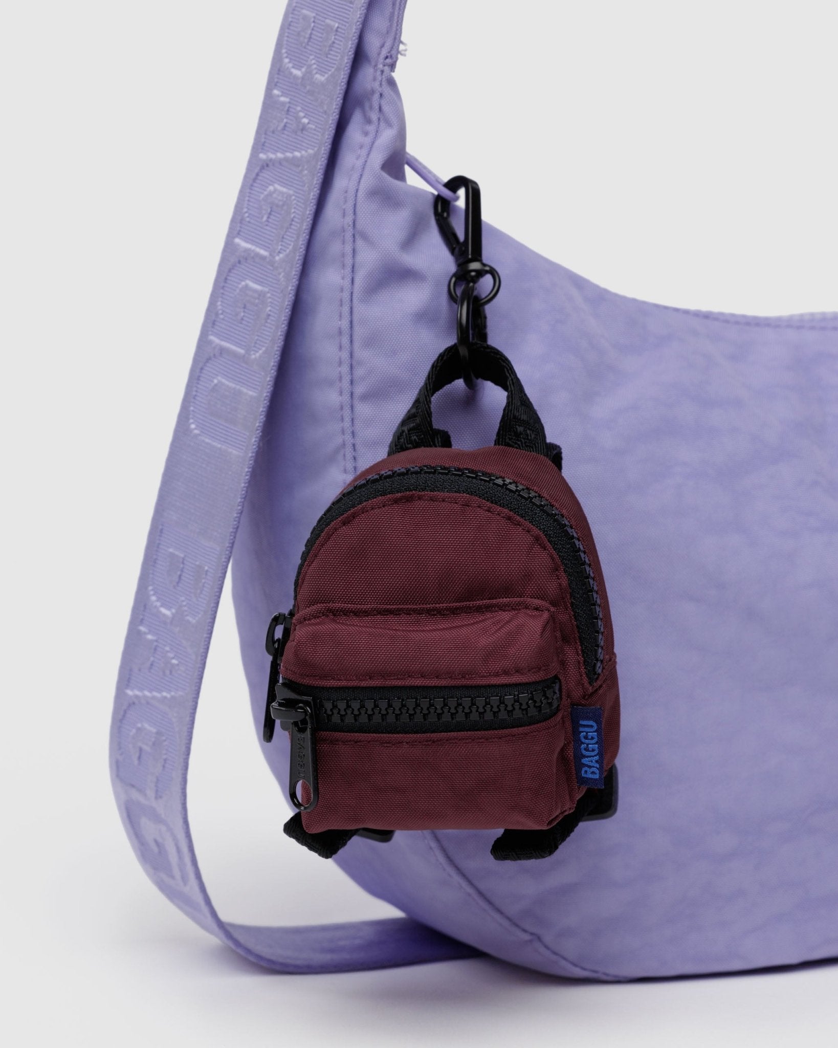 Backpack bag charm in mahogany attached to purple crossbody bag zip.