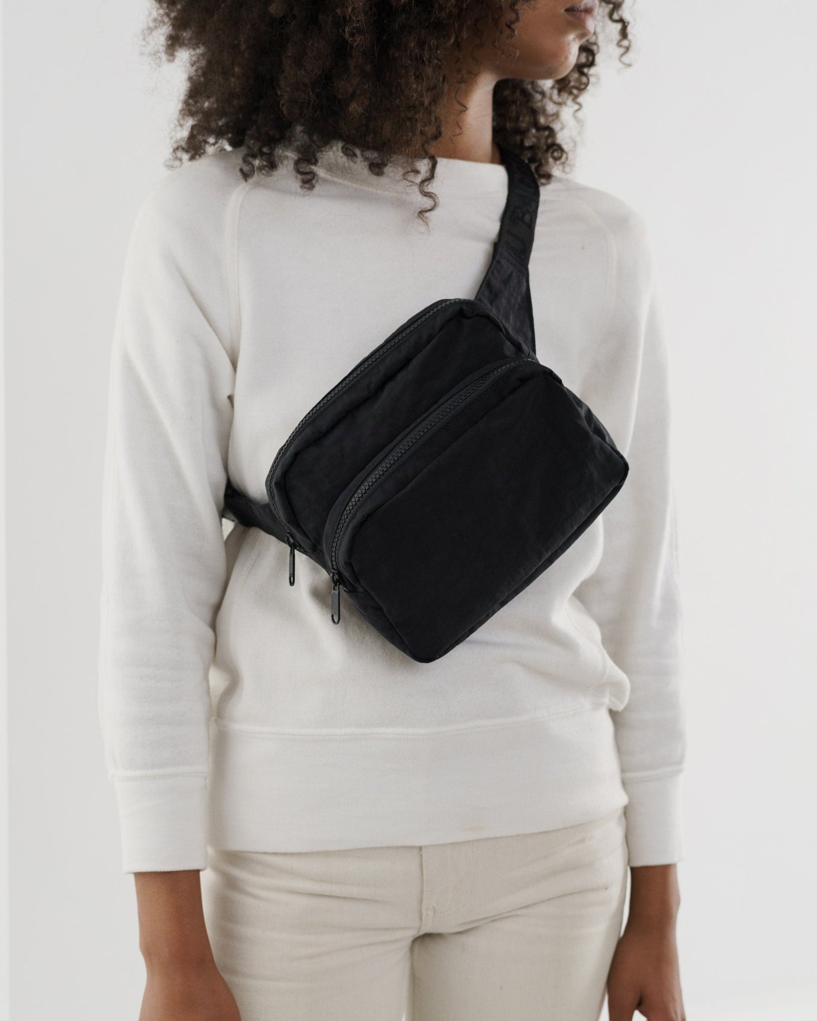 Person wearing a black crossbody fanny pack with two zip compartments.