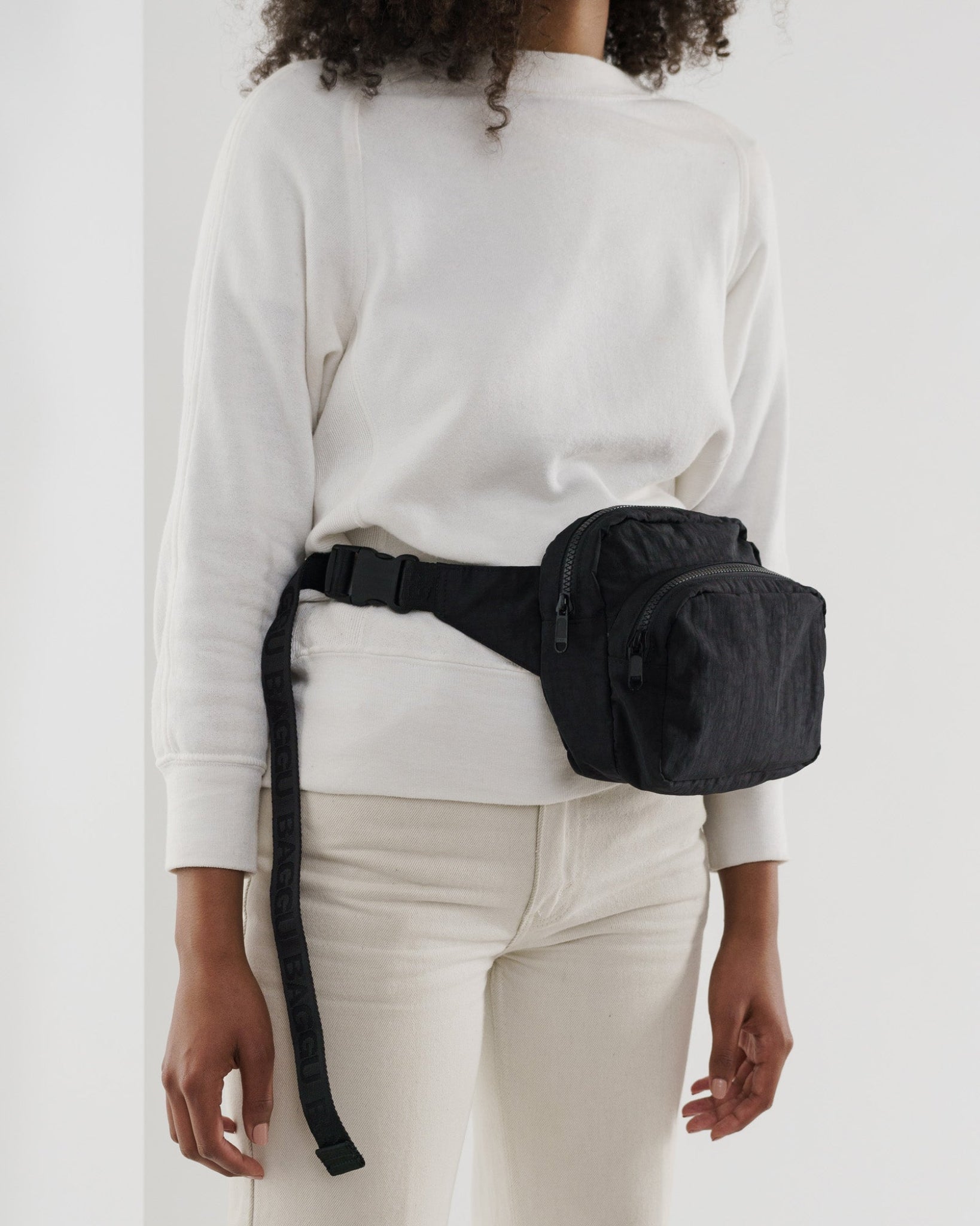 Person wearing a black fanny pack around waist with adjustable strap.
