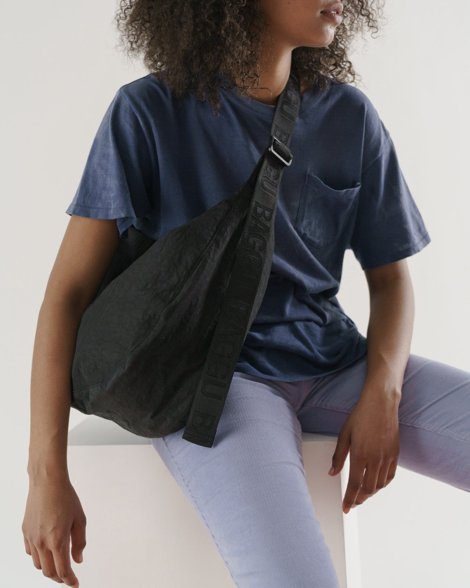 Woman sitting with the large black crescent bag on shoulder with an adjustable shoulder strap- ANNIE.G