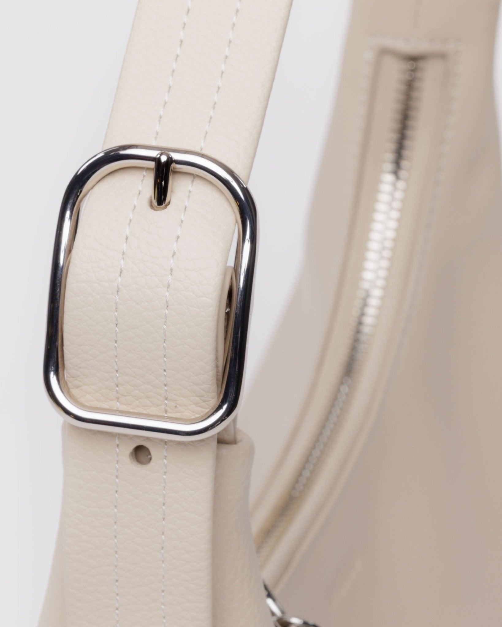 Close up of silver buckle hardware on adjustable shoulder strap of mini recycled leather bag in stone