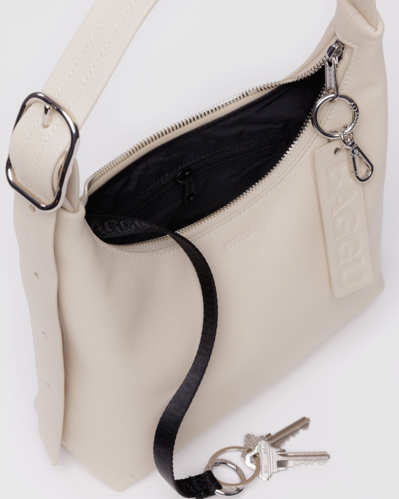 Top zip open showing inside black nylon interior lining, keyleash with keys attached and zip compartment of Baggu Mini Recycled Leather Shoulder Bag in stone