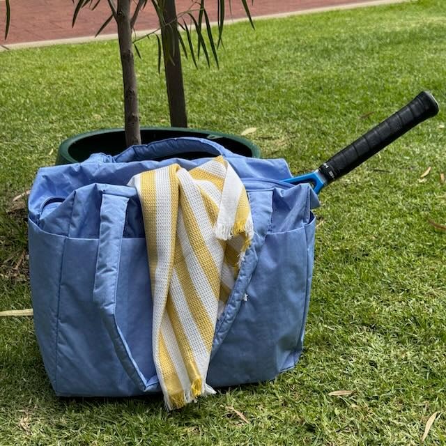 A blue Baggu Small Cloud Carry On used as a tennis bag with racquet and towel.