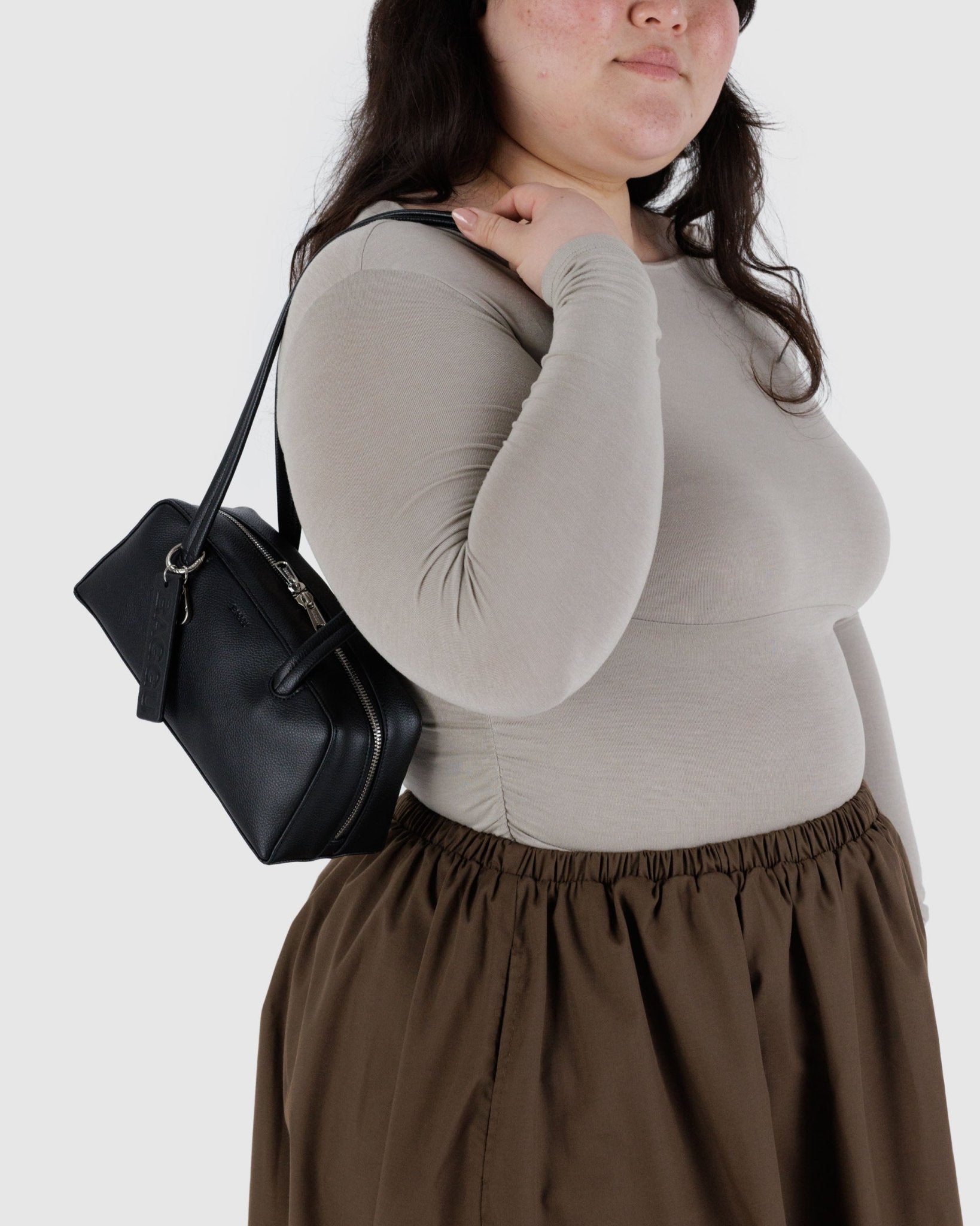 Woman carrying a small black leather bowler bag on shoulder.