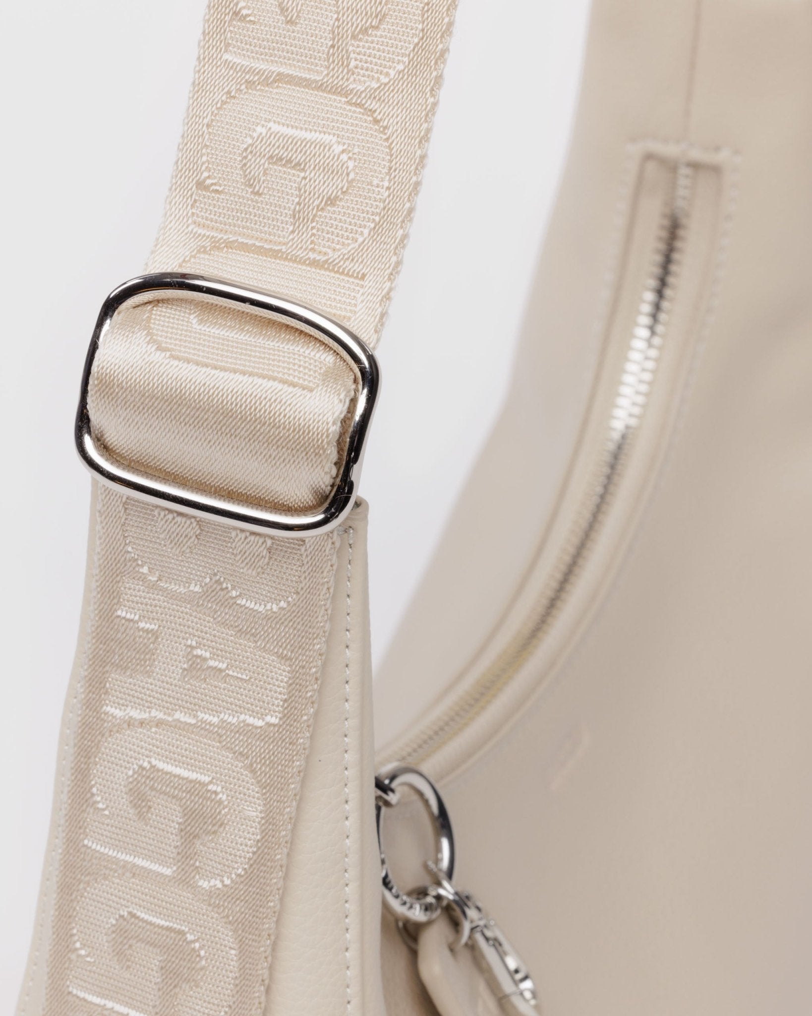 Stone tonal adjustable strap and silver metal hardware on a small recycled leather crescent bag. 