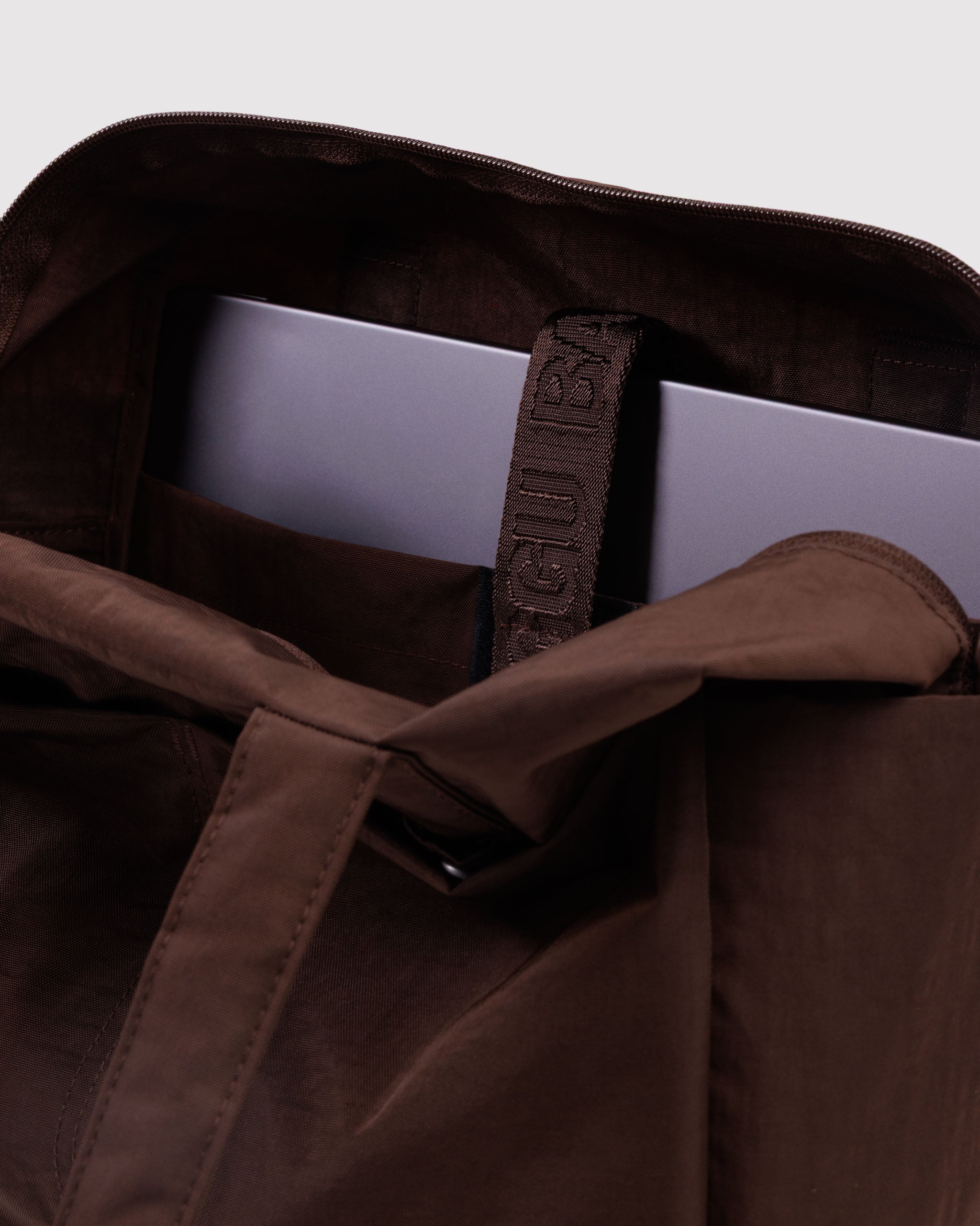Brown bag with a laptop inside in a tech pocket with secure strap closure.