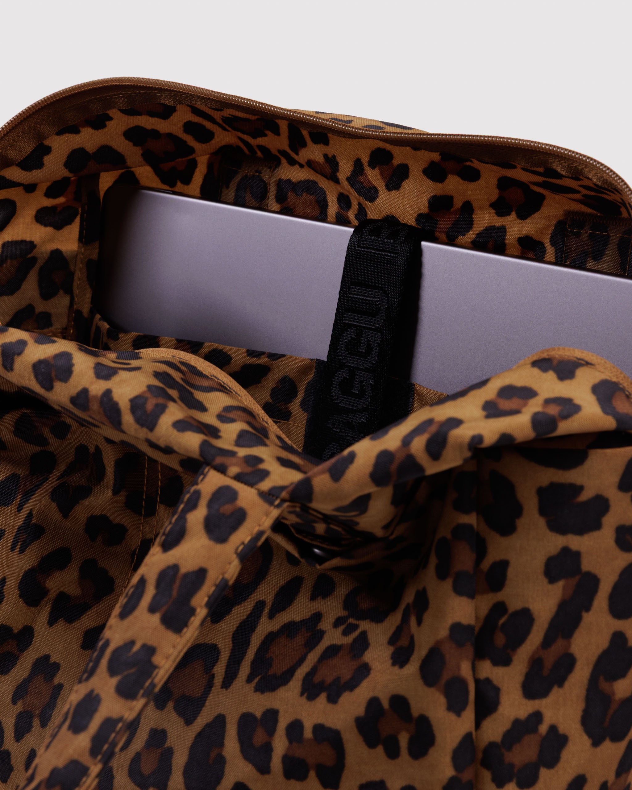 Leopard print bag with a visible laptop inside a tech pocket with secure strap closure.
