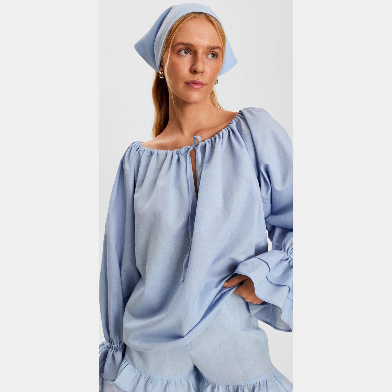 Woman wearing a light blue off-shoulder top with ruffled details on a white background