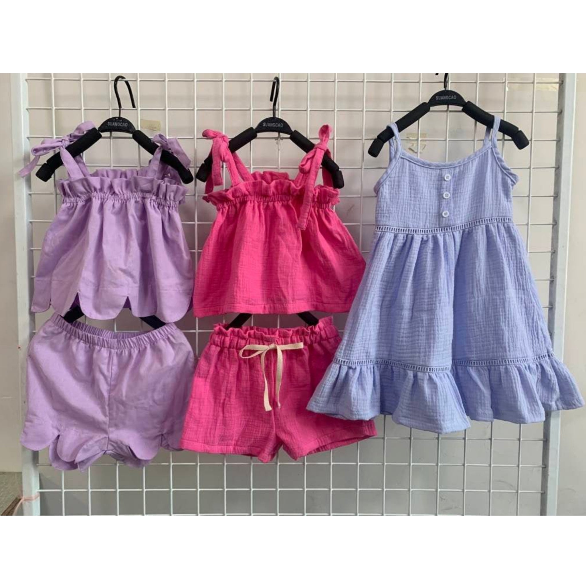Purple shorts and top set, pink shorts and top set and a blue dress hanging on a screen.
