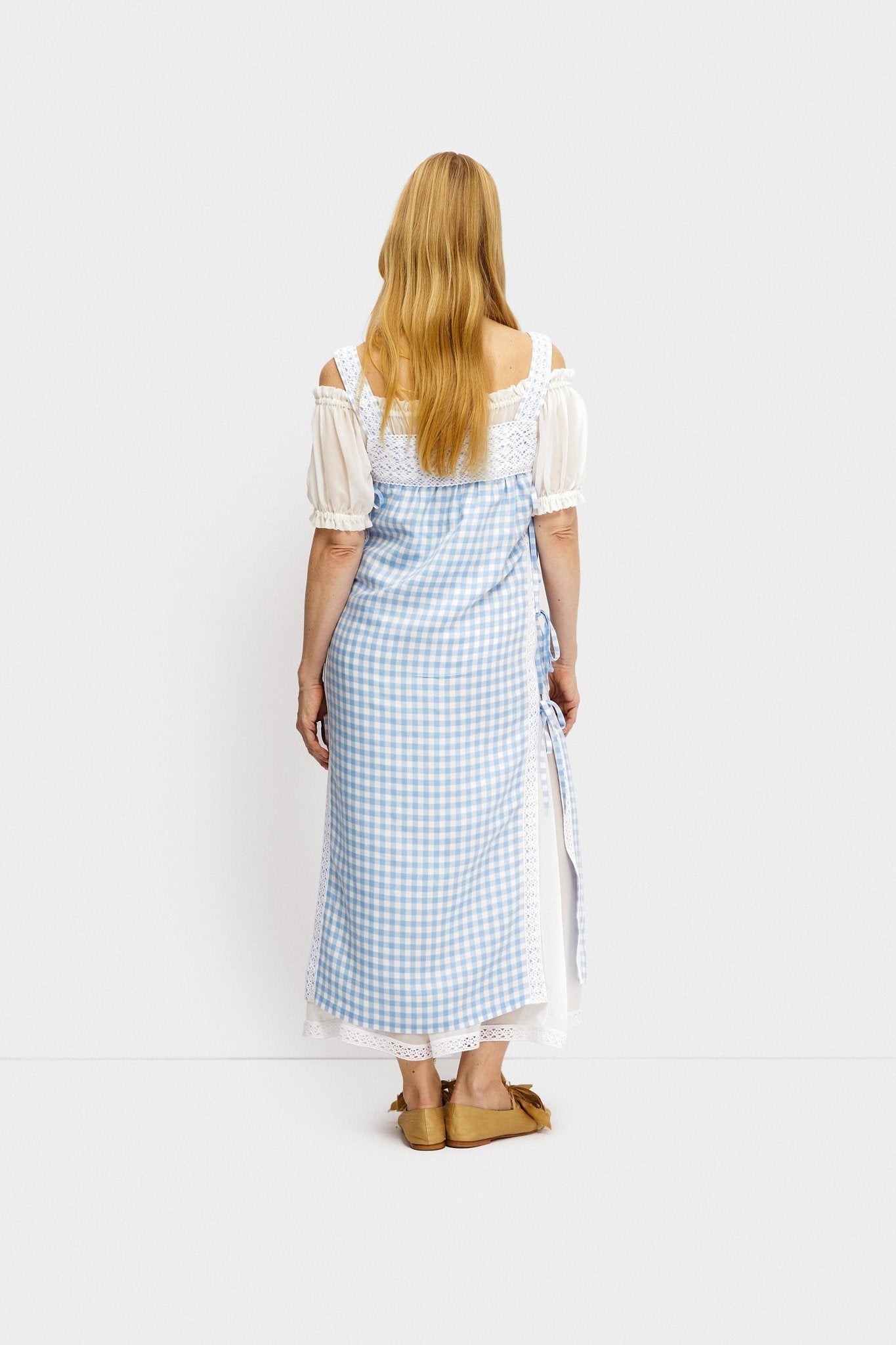 Back of a woman wearing a white short sleeve under dress layered with a blue and white checked tunic.