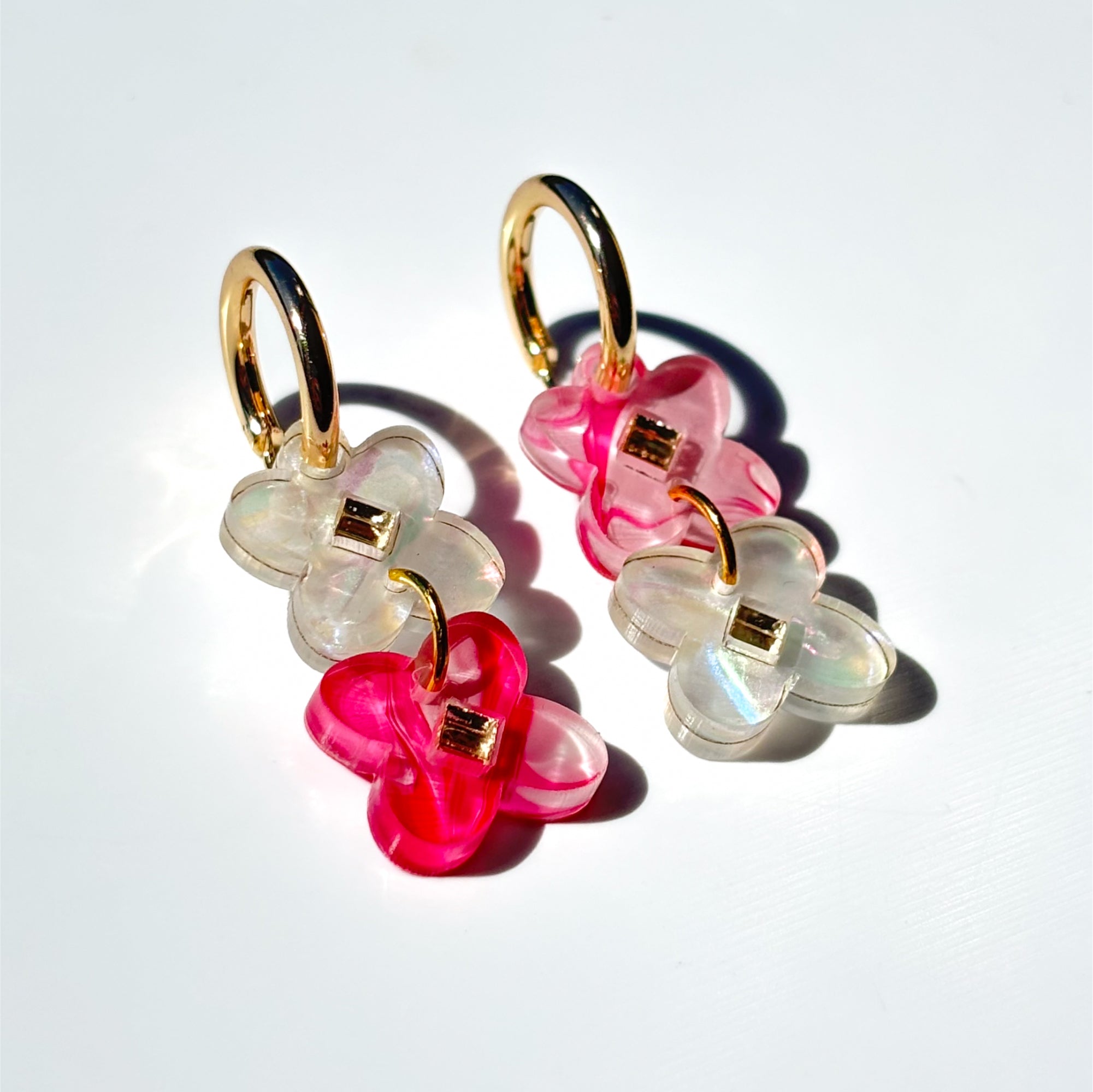 Two sweet clover acrylic flowers inset with gold mirror diamond in vibrant pink and white swirl acrylic on small gold hoops.