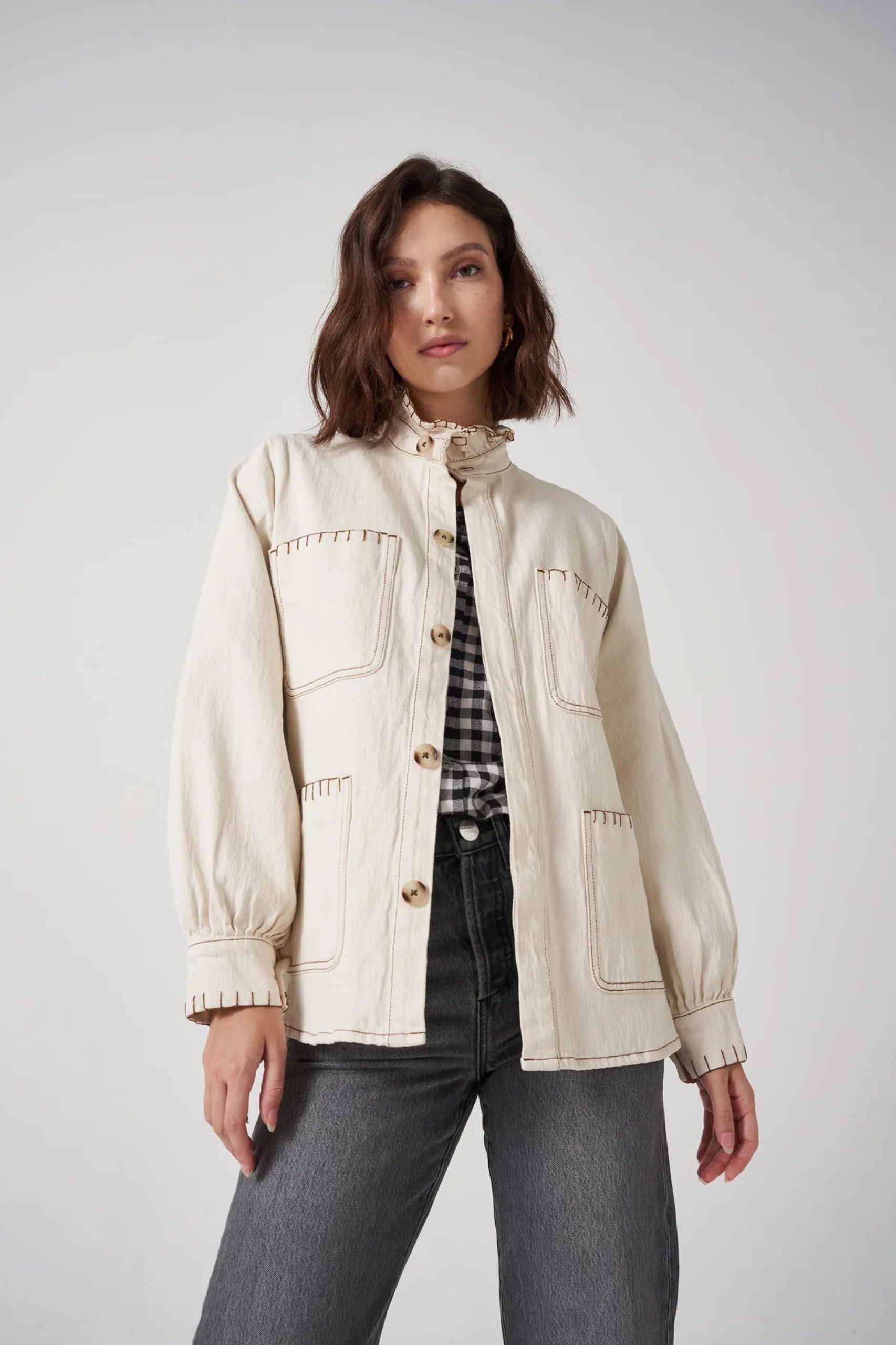 Woman wearing a cream jacket with buttons and patch pockets over a shirt and denim jeans.