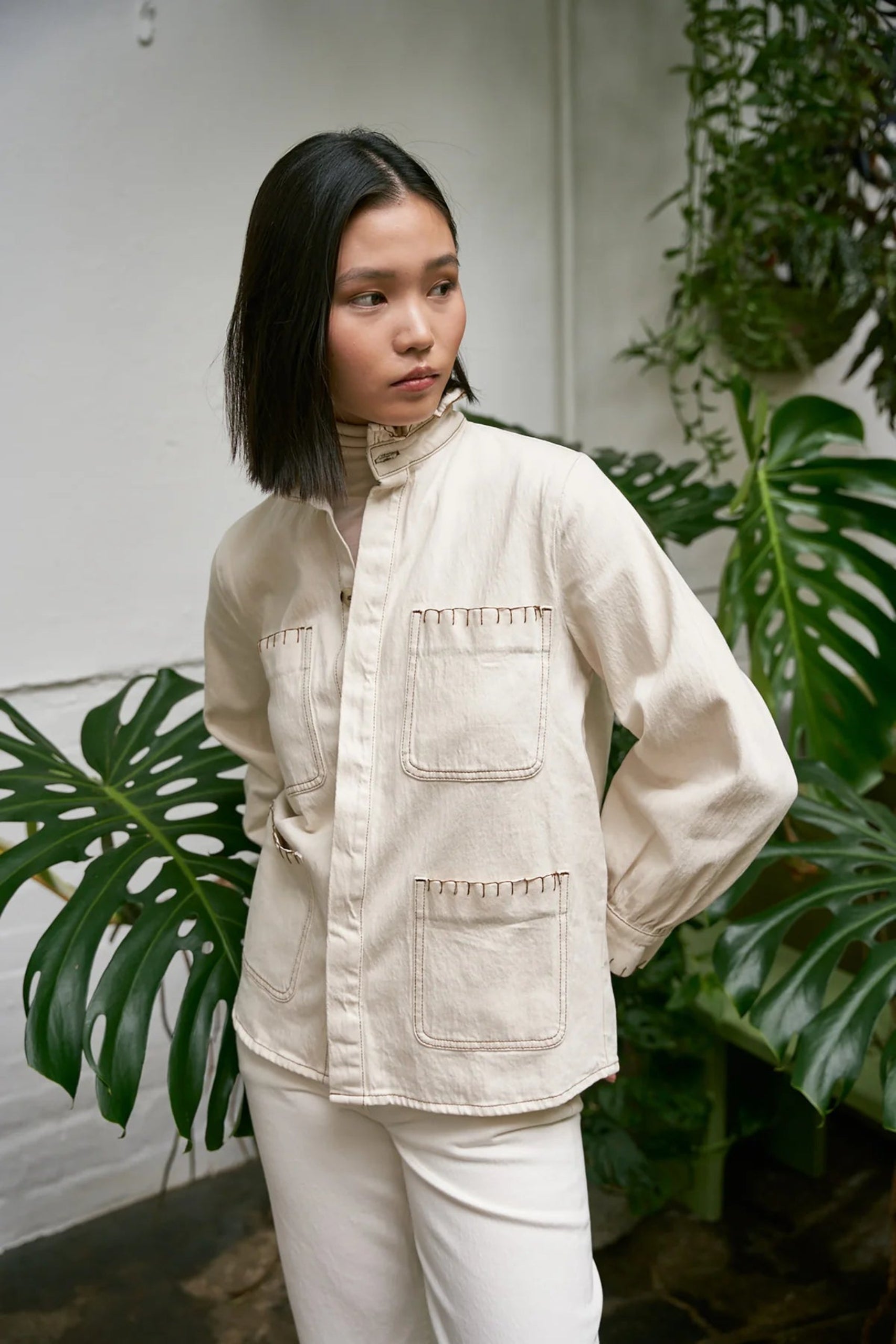 Buttons done up on front of cream jacket worn by a woman over white jeans - ANNIE.G