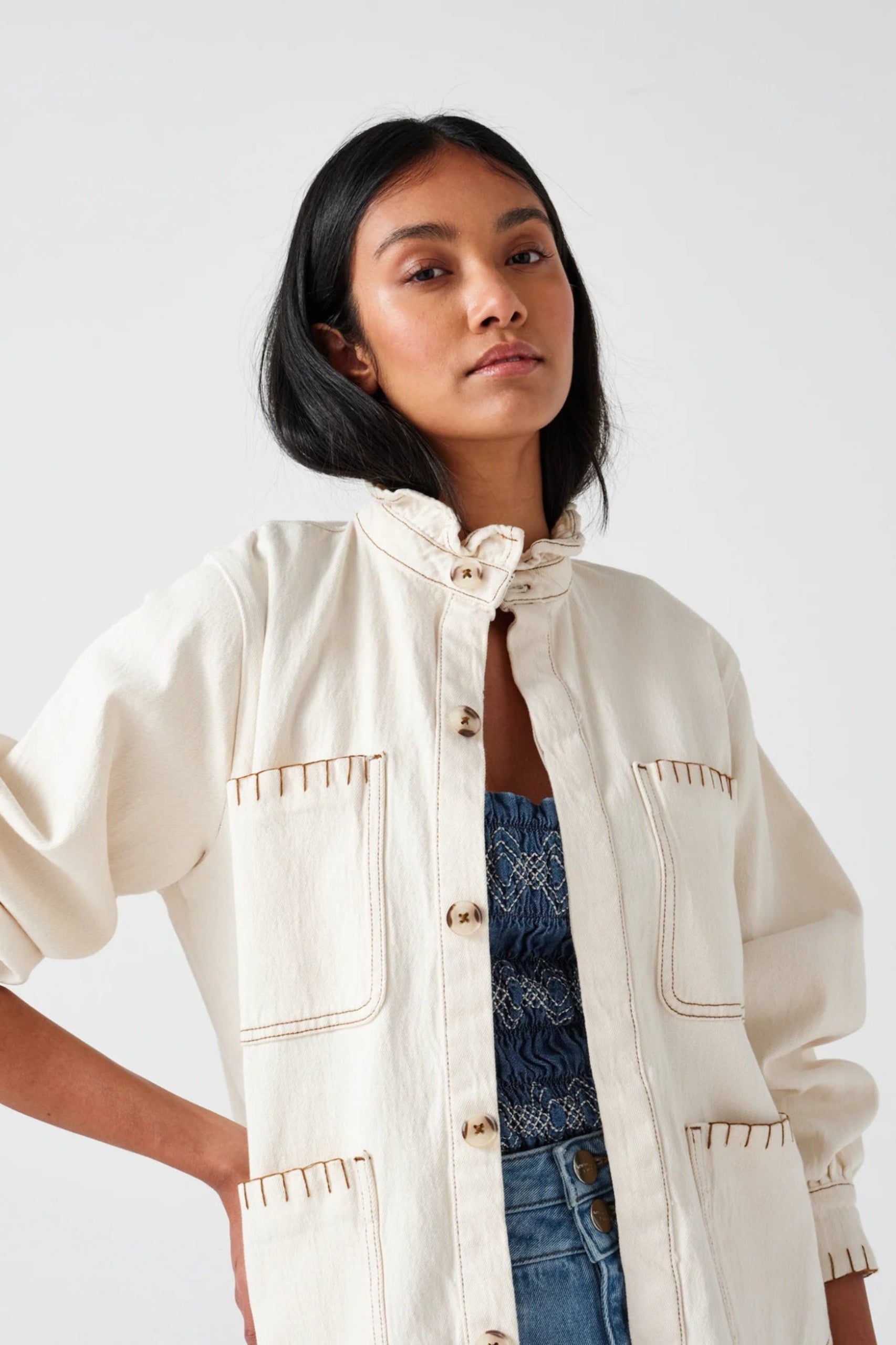 Close up of blanket stitch detail on a cream jacket being worn by a woman.