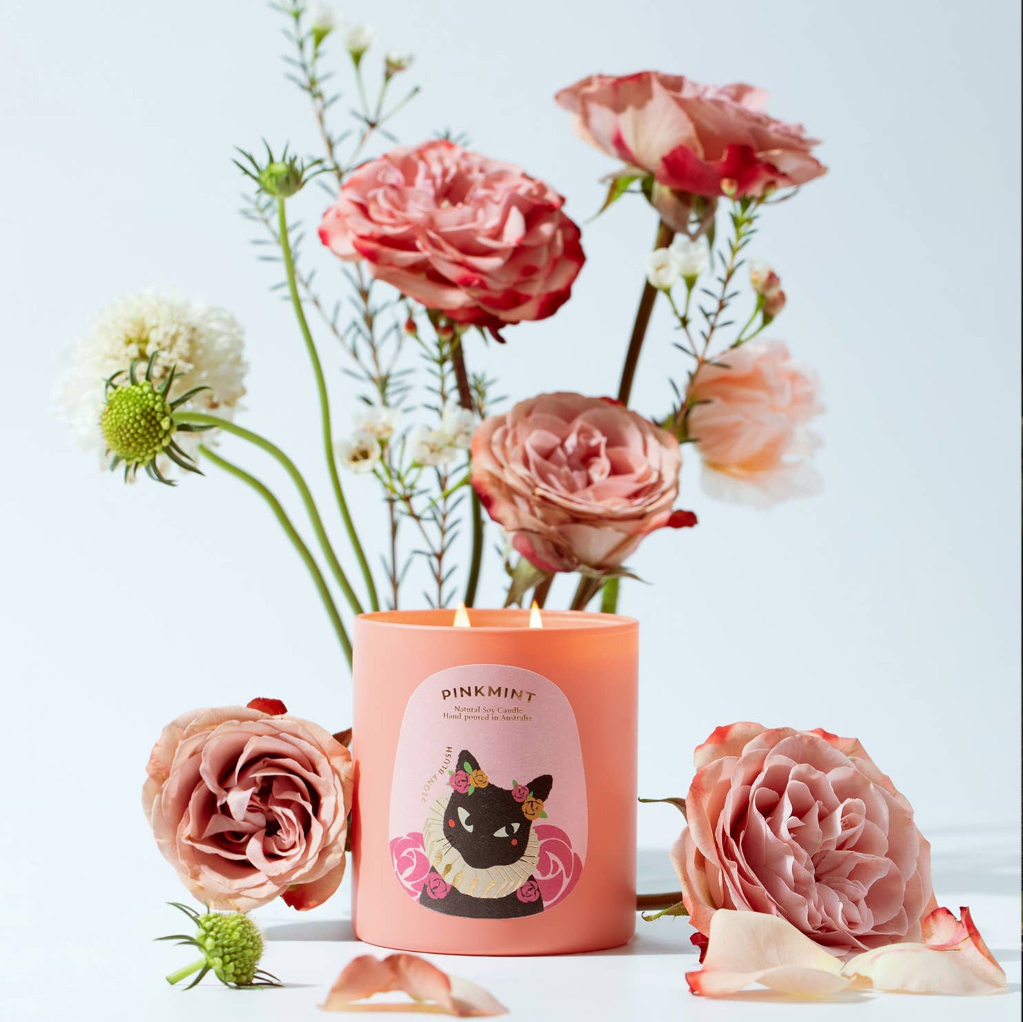 Pink flowers surrounding a pink candle jar with double wick lit and a pink label, 250ml - ANNIE.G