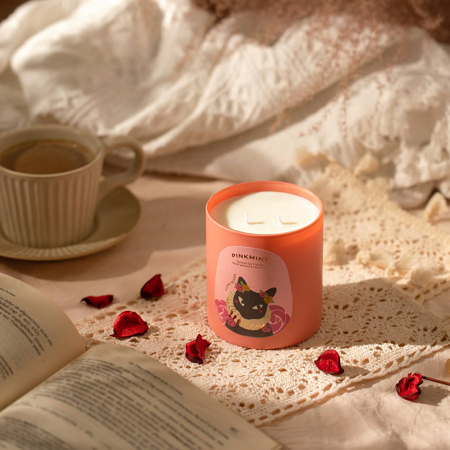 Pink candle jar on a bed with book and a coffee cup - ANNIE.G
