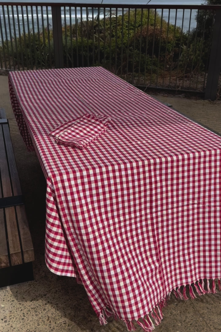 red-gingham-cotton-tablecloth-handknotted-edge-on-picnic-table-at-beach-blowing-in-the-wind
