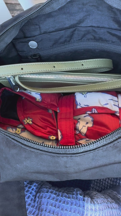 Movie of inside the black everyday cloud bag storing a green pochette purse and puffy picnic blanket with white bunnies and a navy towel beside the bag.