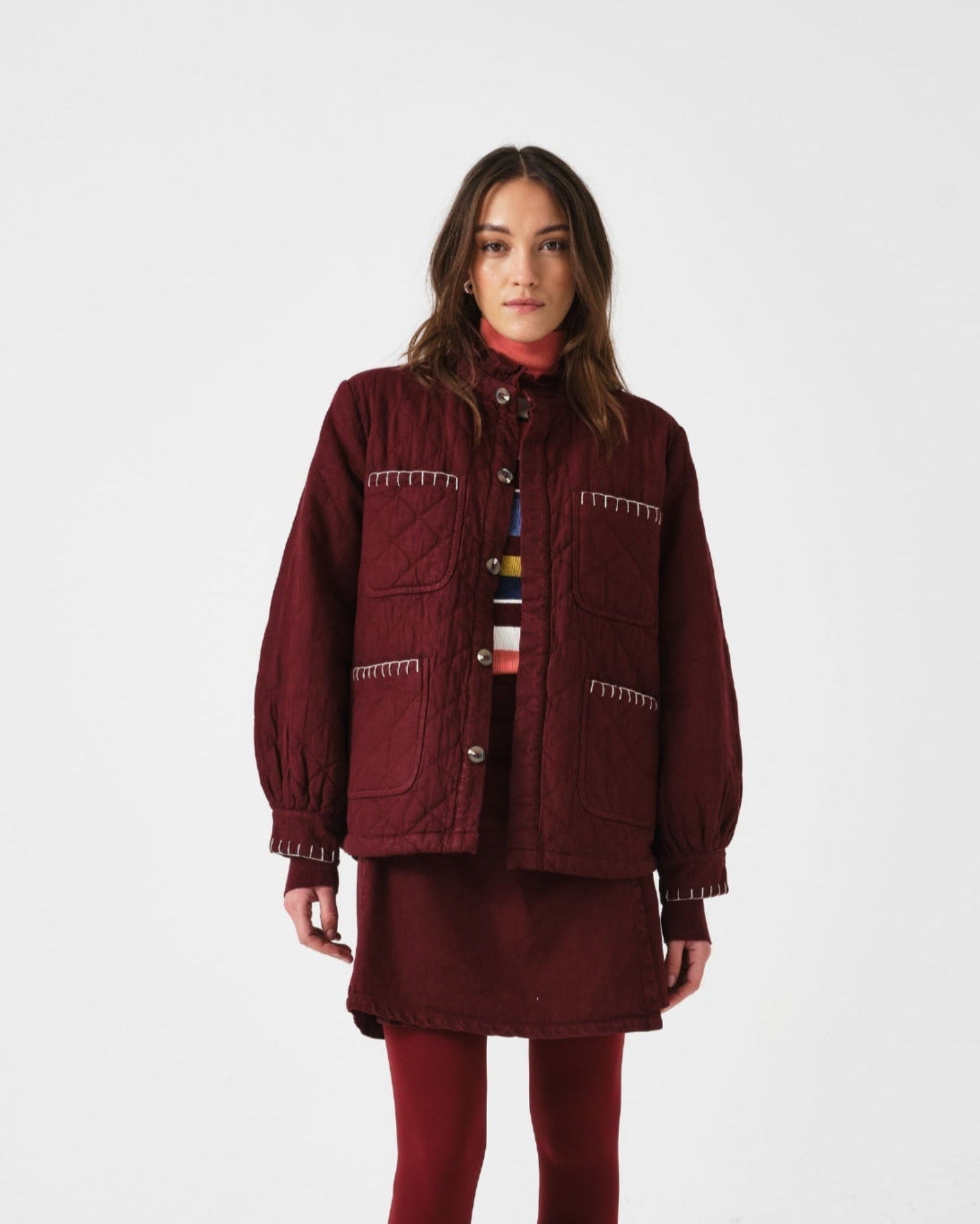 Woman wearing a burgundy outfit with a quilted jacket and mini skirt.