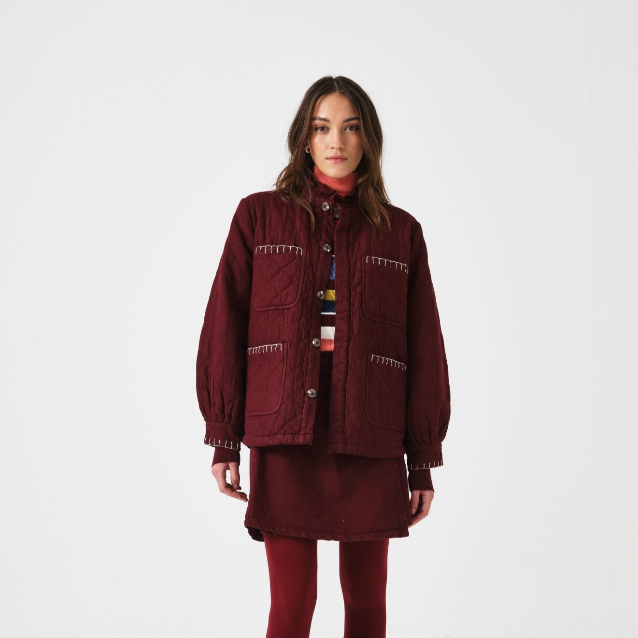 Woman wearing a burgundy outfit with a quilted jacket and mini skirt.