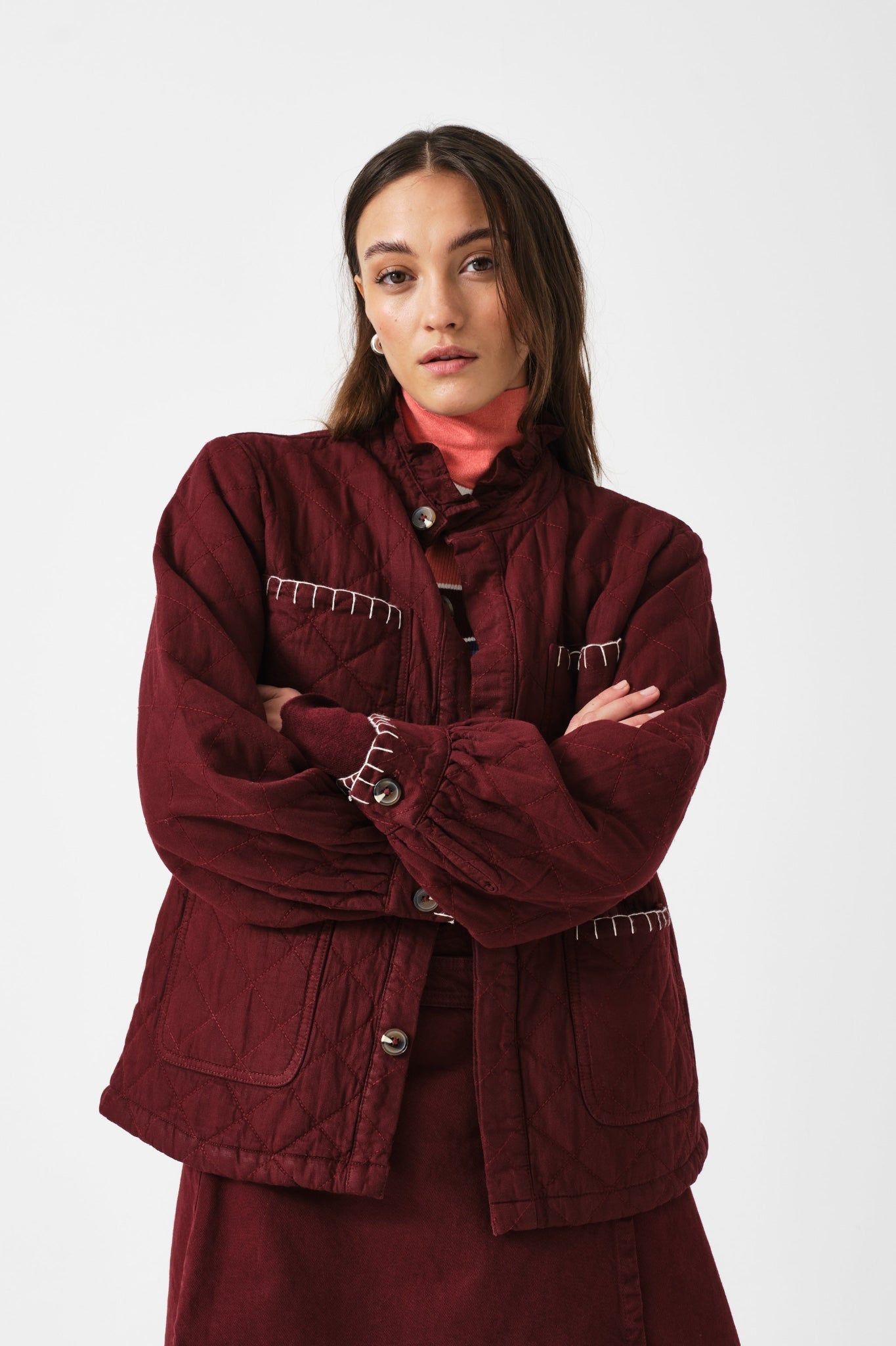 Woman with arms crossed wearing a burgundy, long sleeve, quilted jacket and matching skirt.