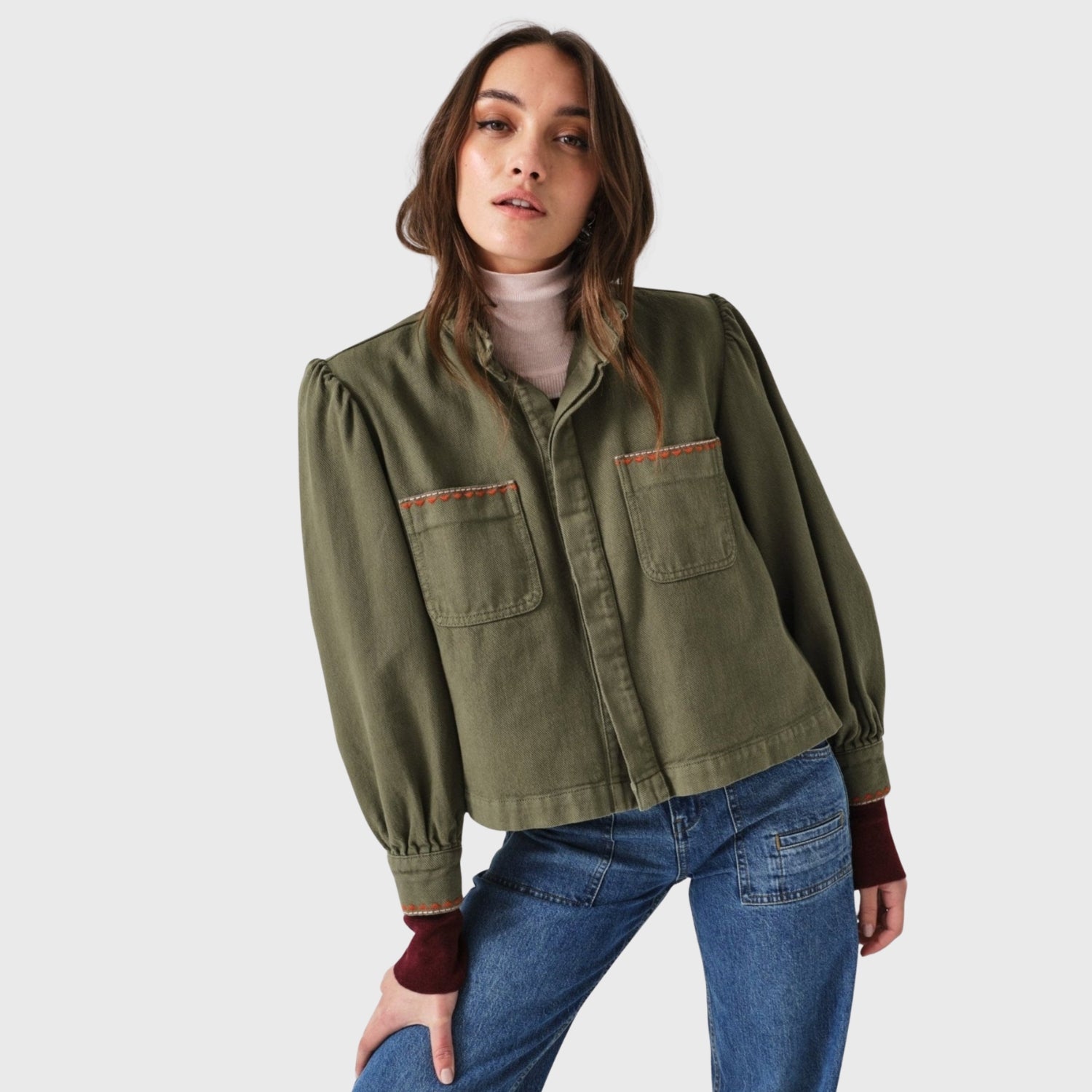 Woman wearing a long sleeve olive green cropped jacket with pockets and embroidery accents on pockets and cuff.