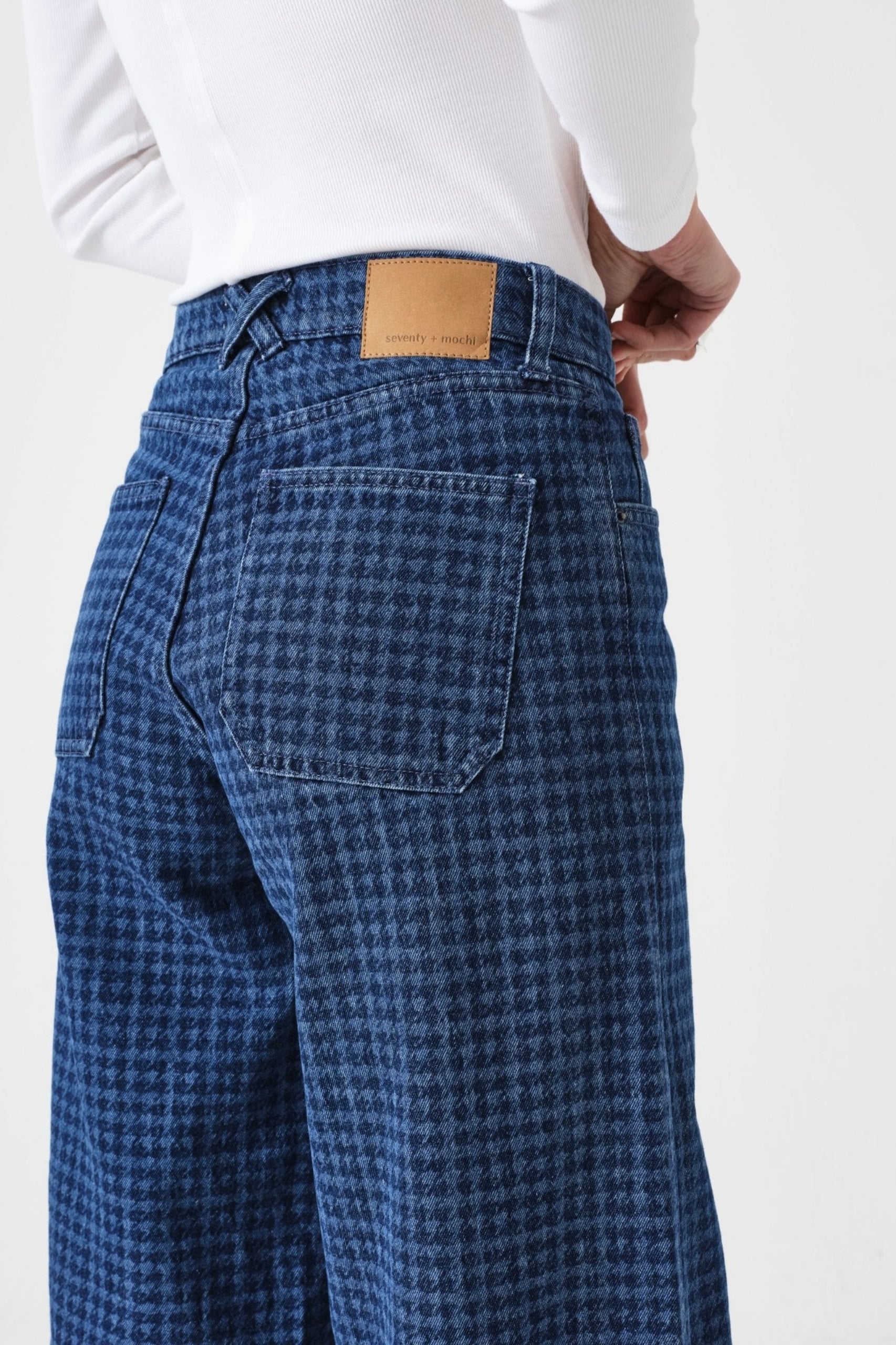 Side of a person wearing blue checkered pants with pockets and belt loops and a white long sleeve shirt.