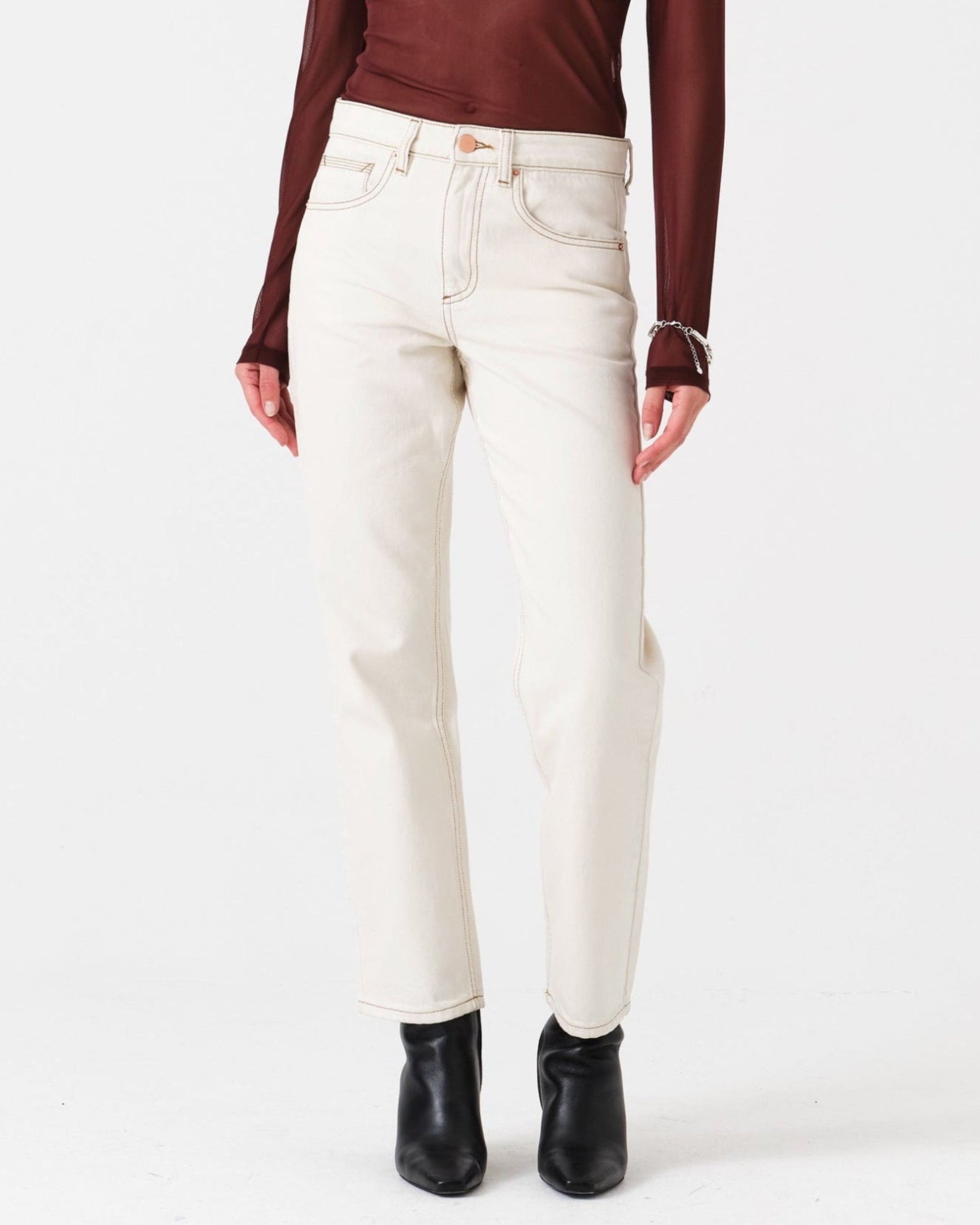 Woman wearing cream straight leg jeans with contrast stitching, a burgundy long sleeve top and boots.