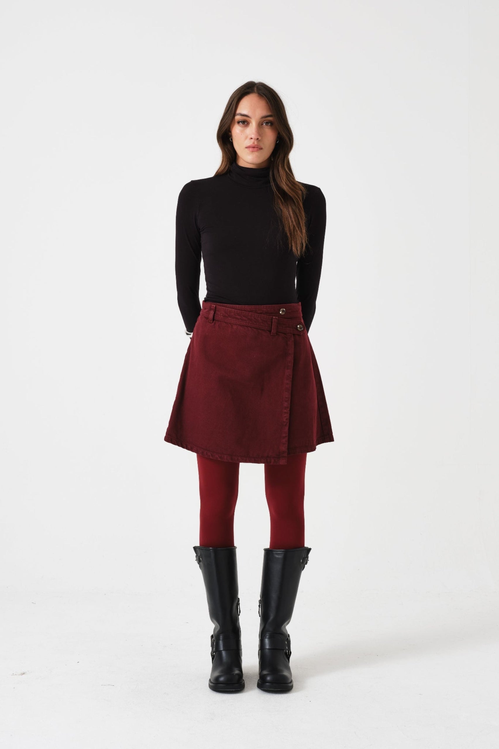 Woman wearing a black turtleneck, mulberry mini wrap skirt, and black boots.