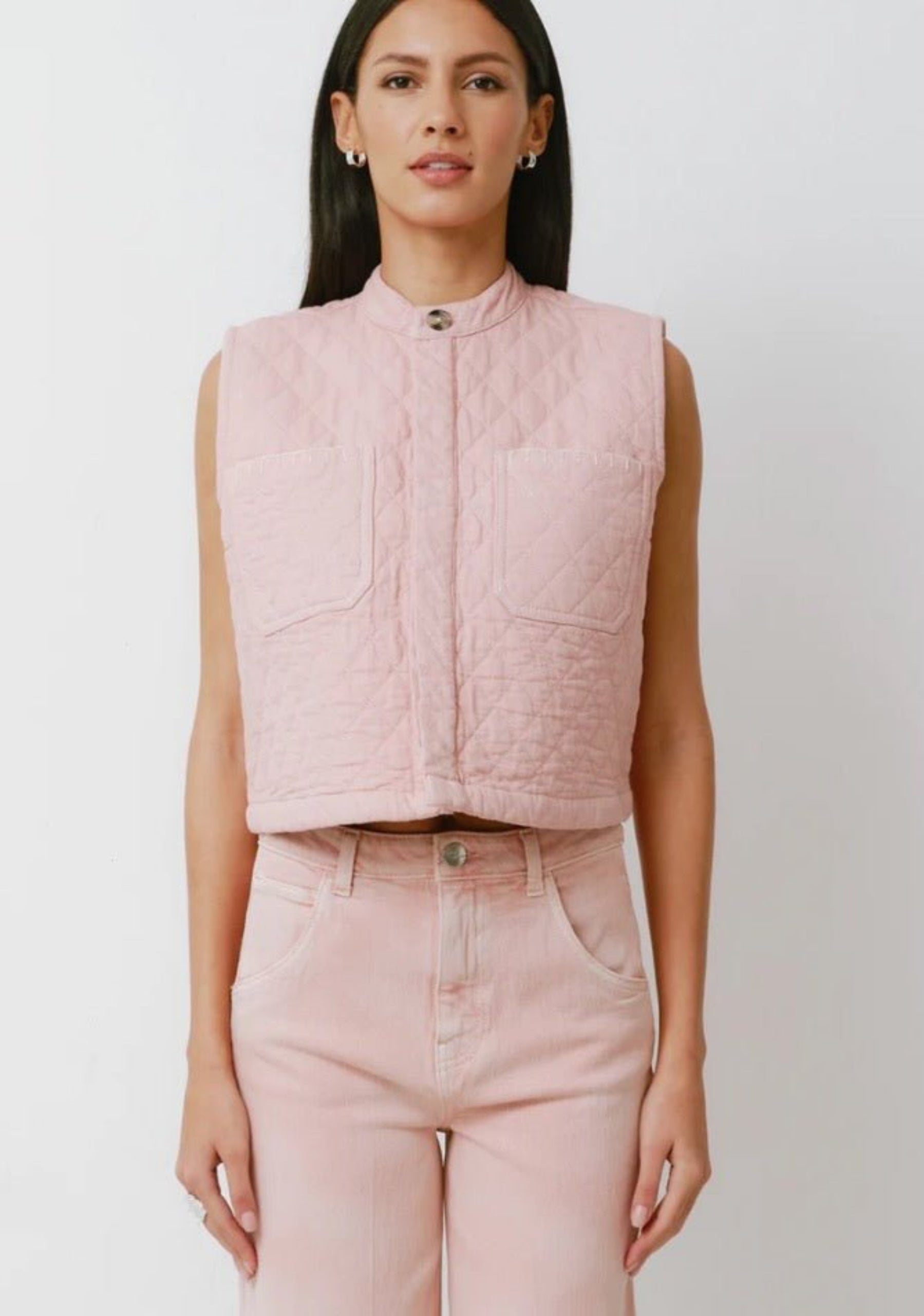 Woman wearing a pink quilted vest buttoned up and pink jeans.