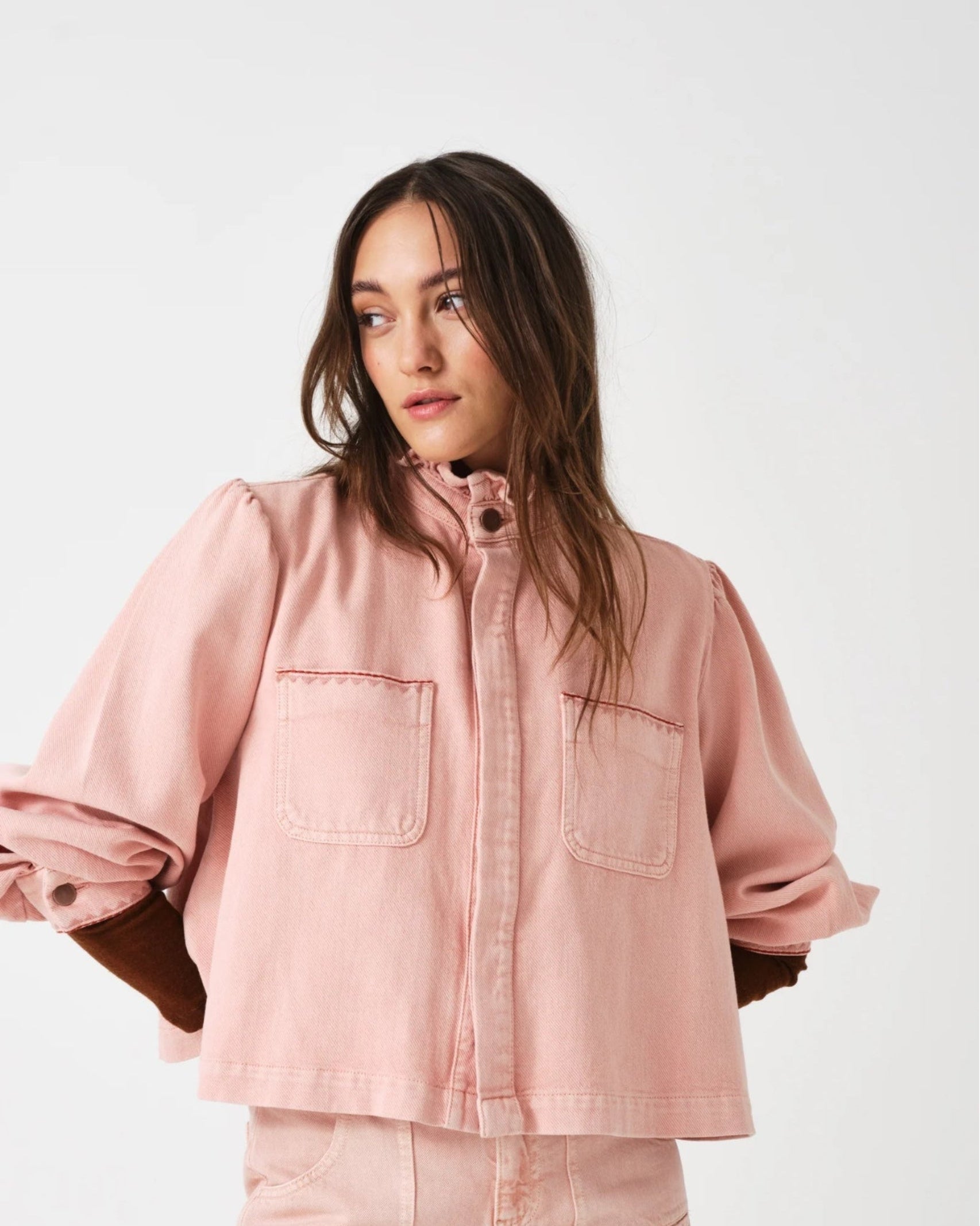 Woman wearing a pink jacket with pockets with pink jeans with arms behind back