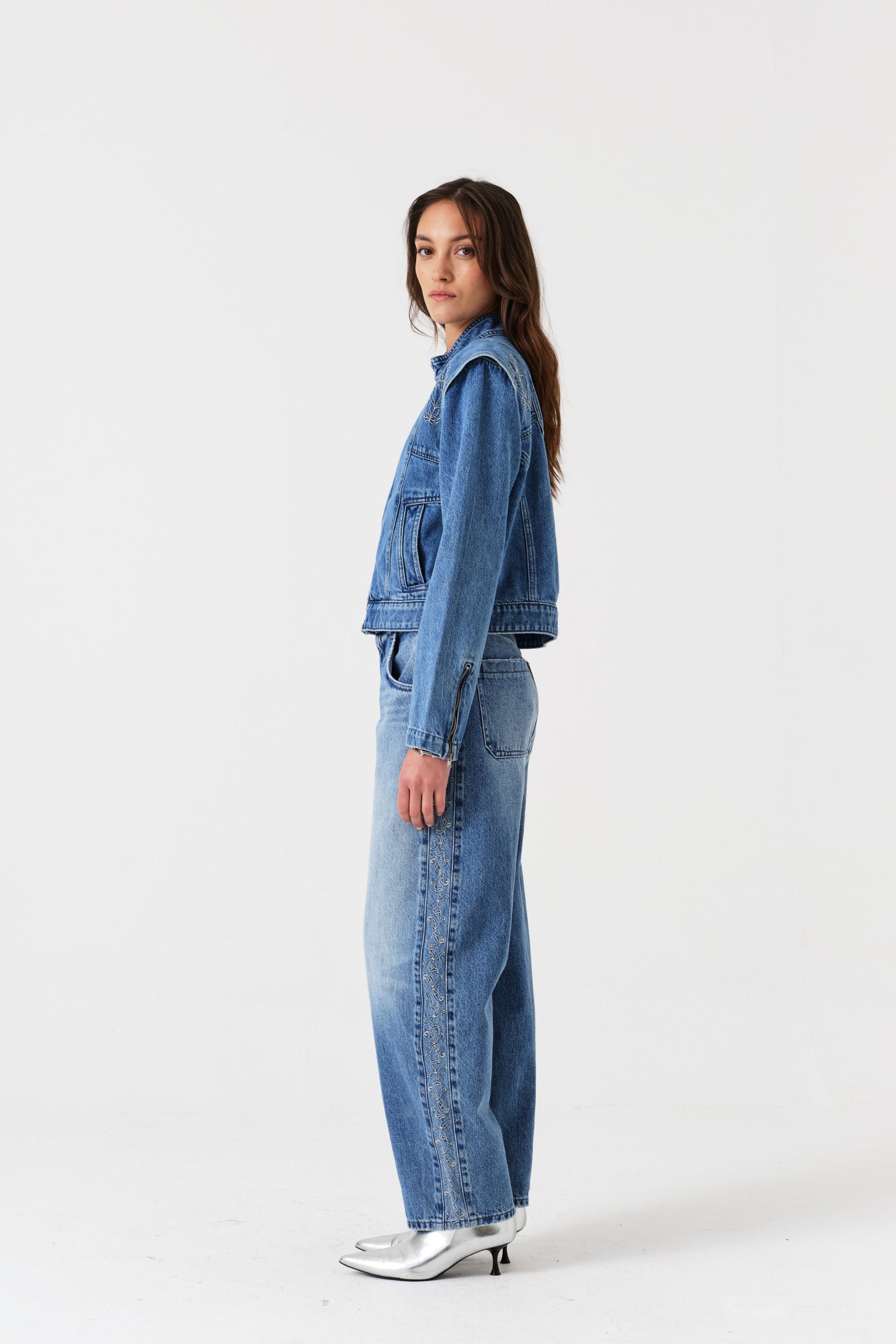 Side view of a woman wearing blue jeans with an embroidered side panel and jacket.