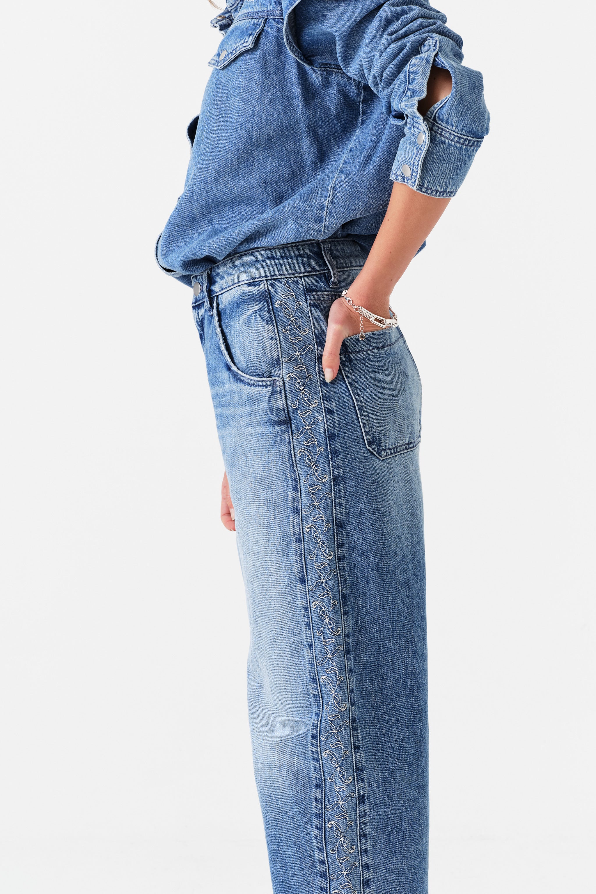 Close up of woman wearing blue jeans with embroidery down side panel and blue denim shirt.
