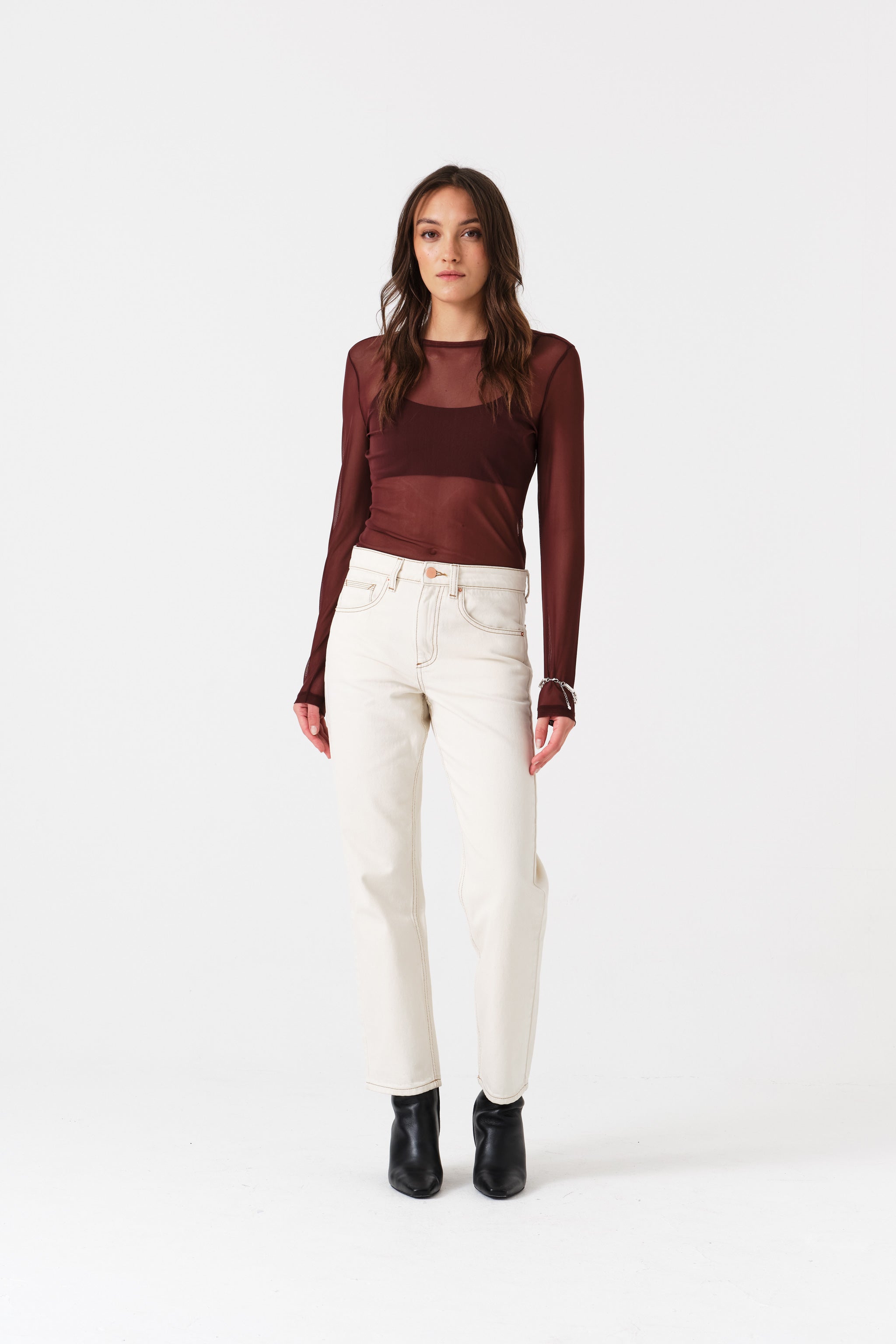 Woman wearing a burgundy sheer top and white jean trousers.