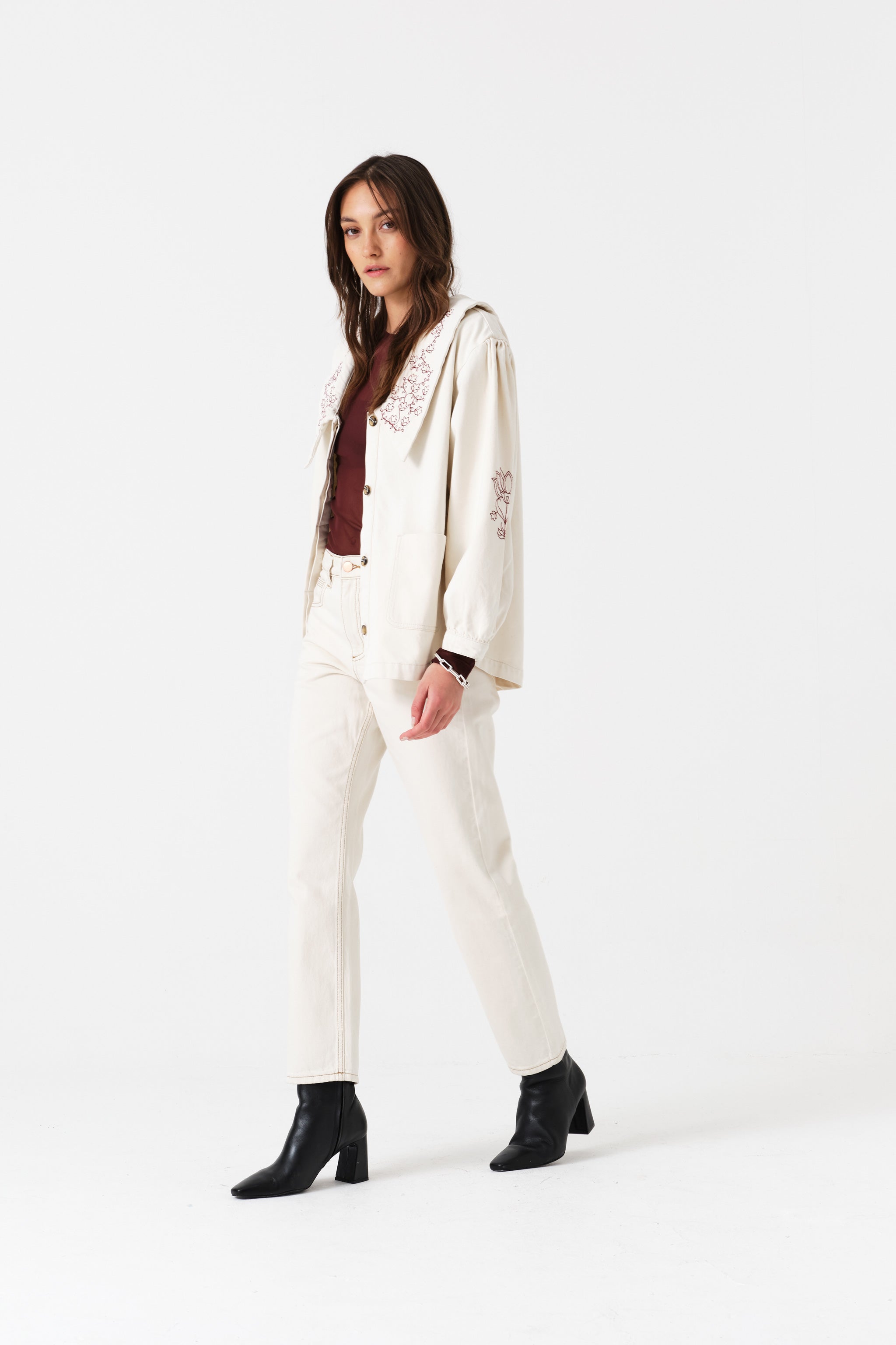 Woman wearing a light cream jacket and jean trousers suit with a brown shirt and black boots.