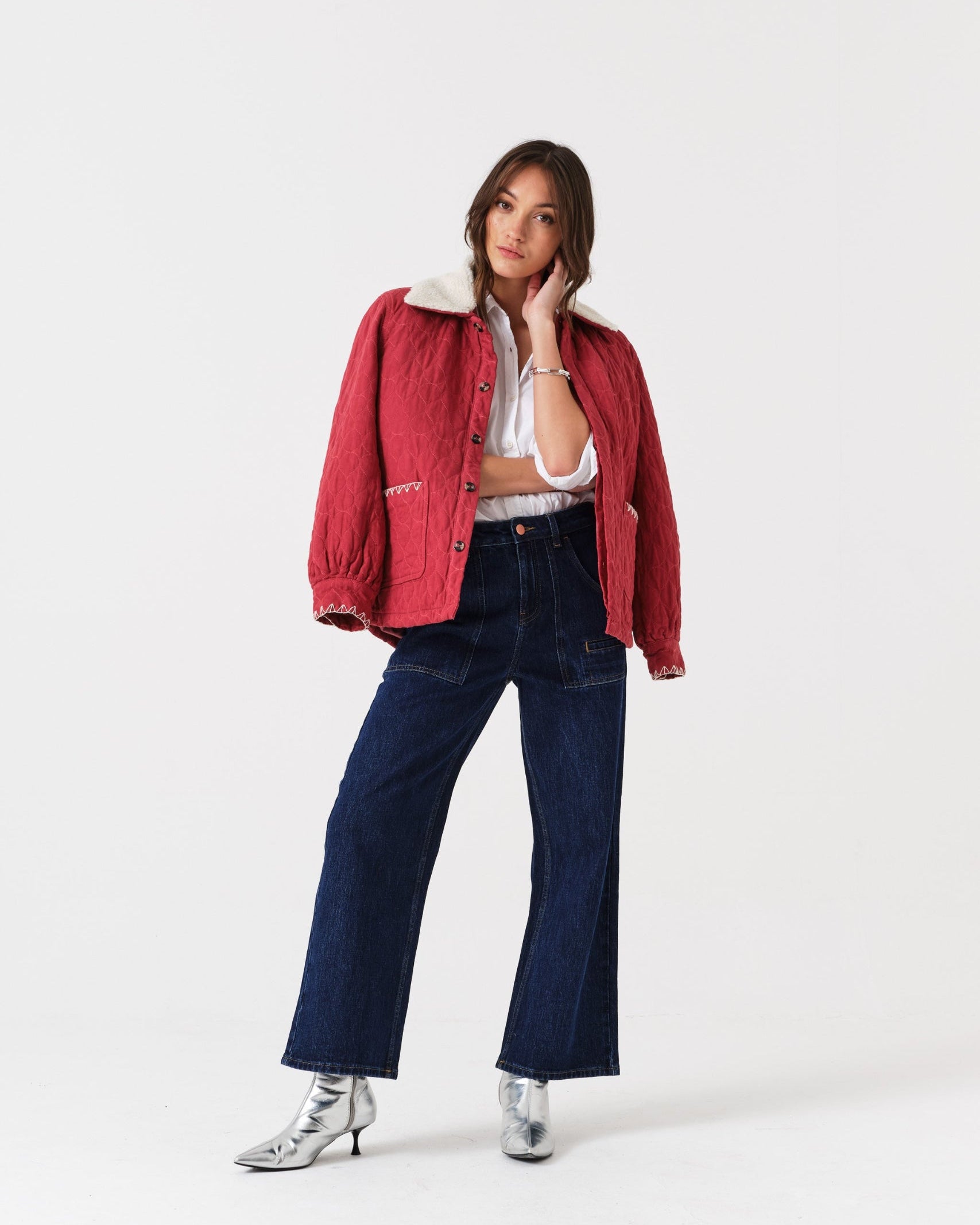 Person wearing a red jacket with white collar, white top, blue cropped jeans, and silver shoes.