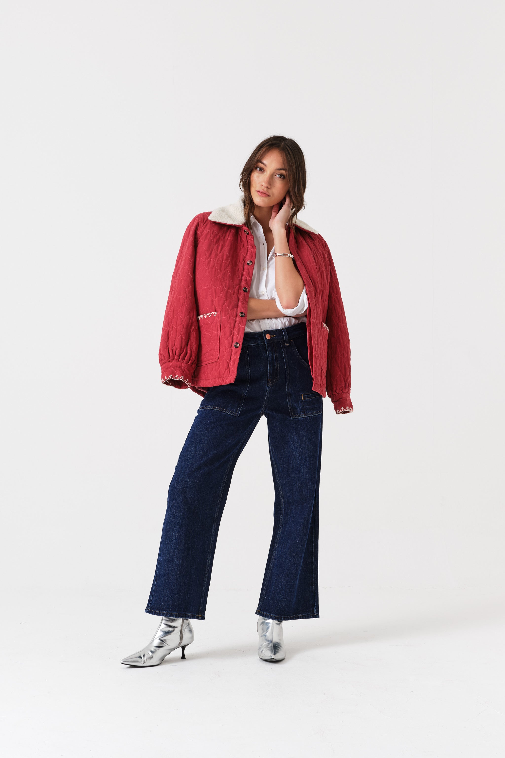 Person wearing a red jacket with white collar, white top, blue cropped jeans, and silver shoes.