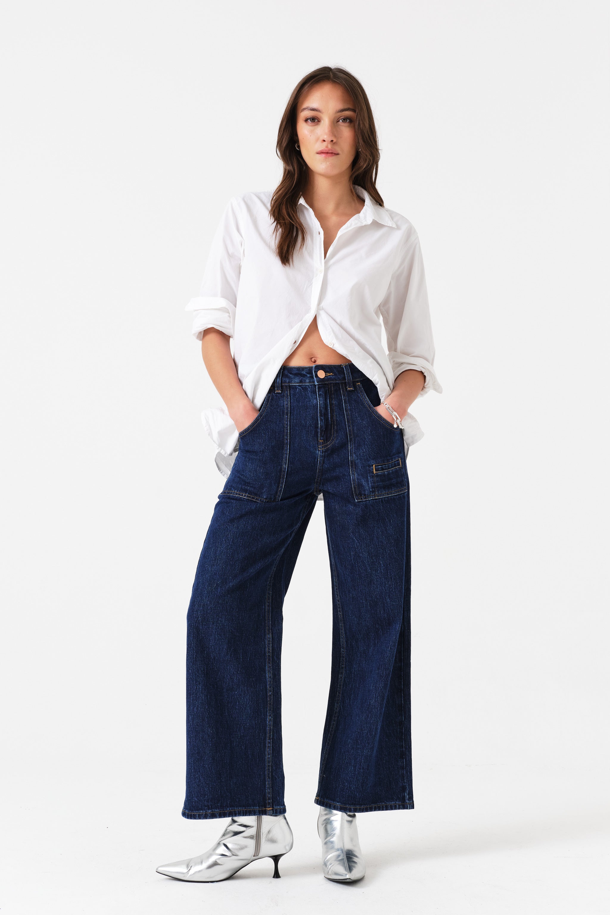 Woman with hands in front pockets of dark blue jeans wearing a white shirt.