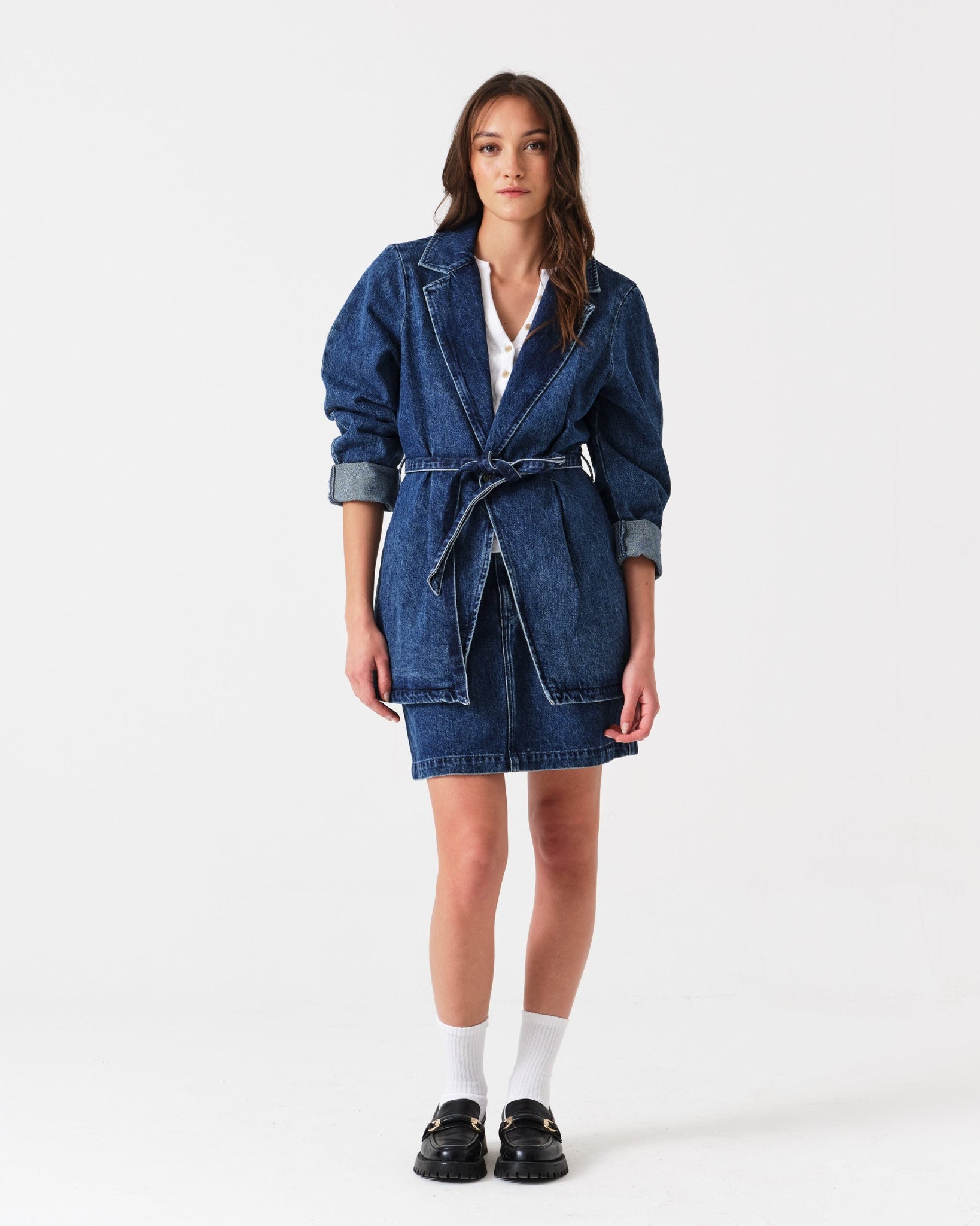 Woman wearing a denim mini skirt and long jacket tied at waist.