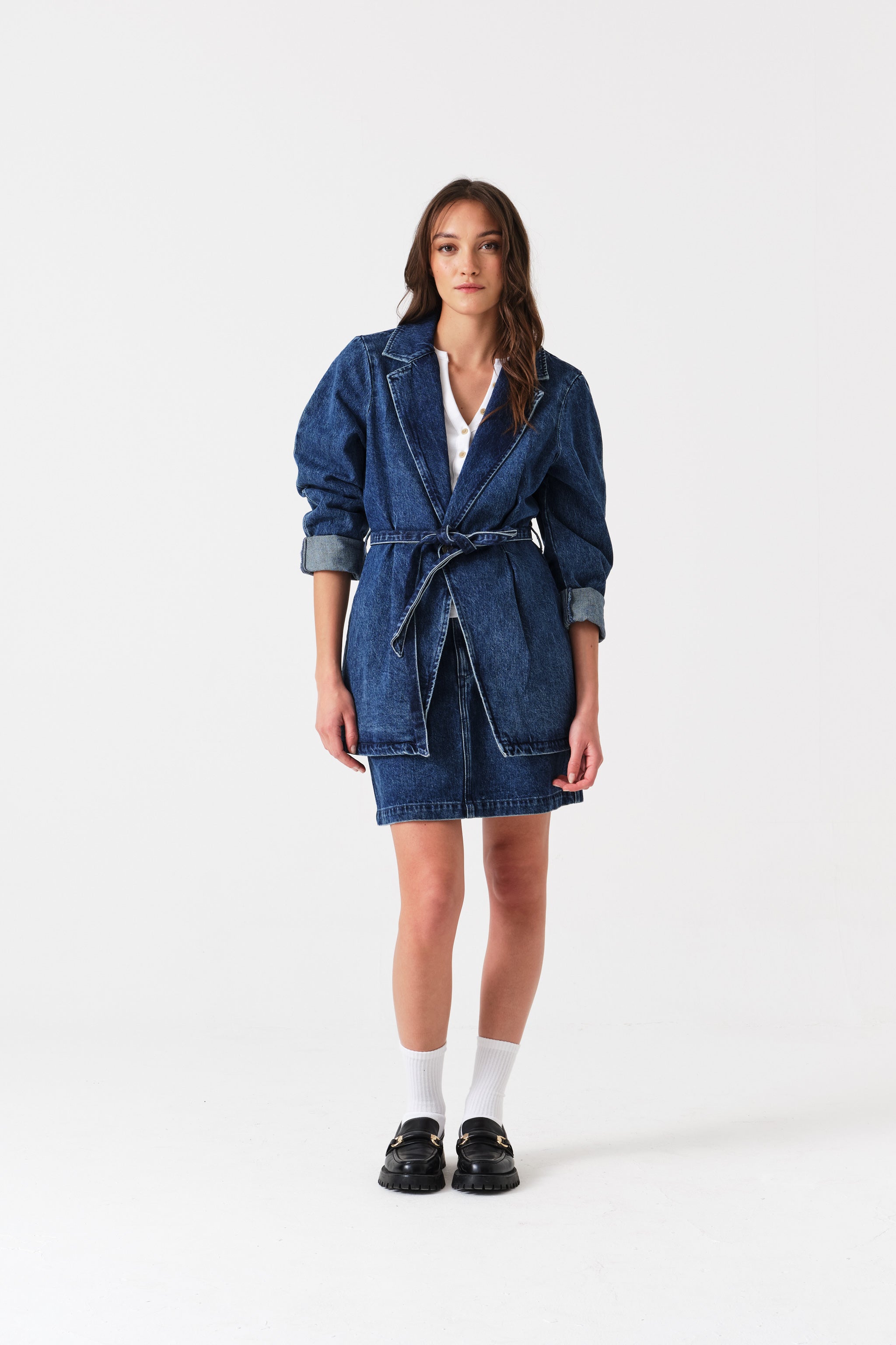 Woman wearing a denim mini skirt and long jacket tied at waist.