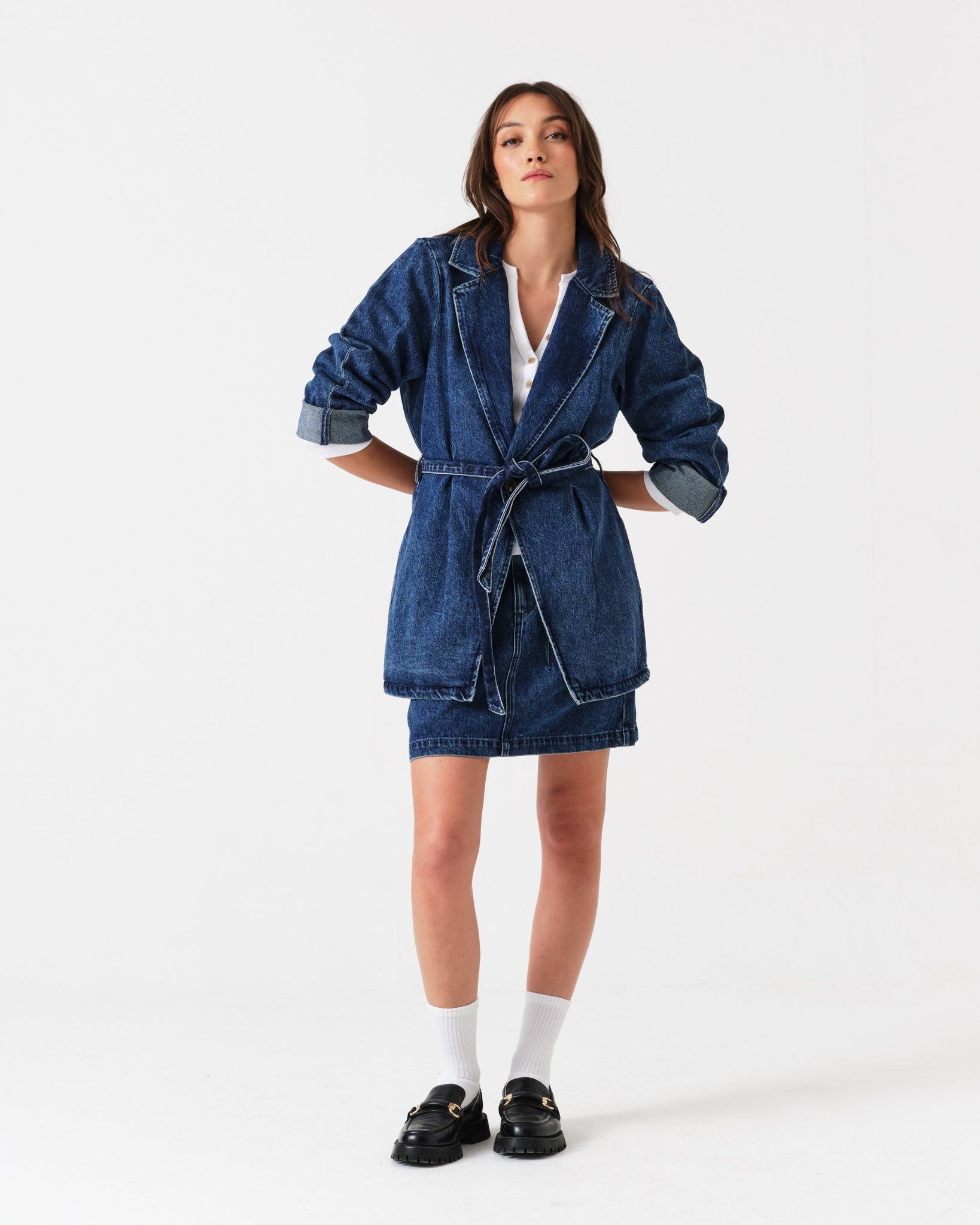 Woman wearing a denim mini skirt and jacket with hands behind back.