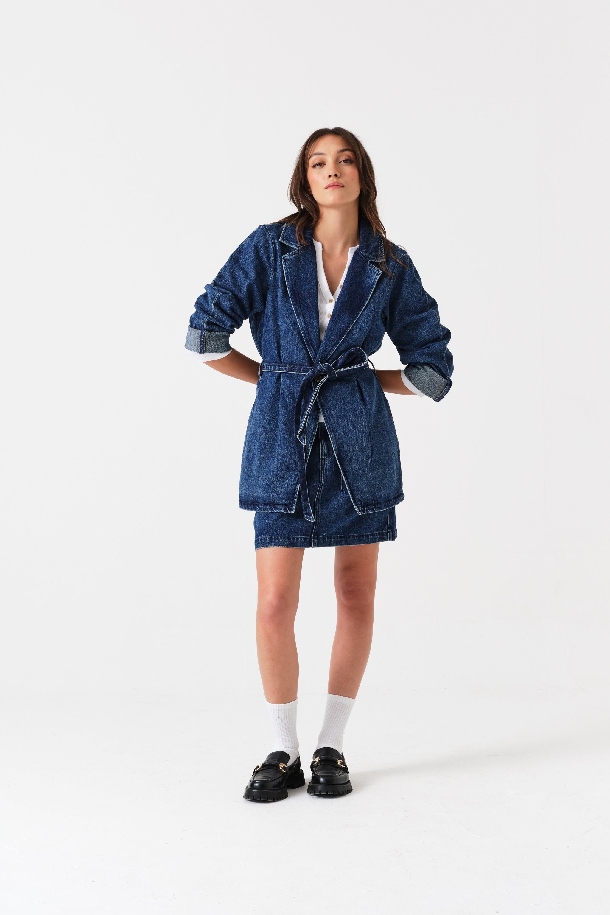 Woman wearing a denim mini skirt and jacket with hands behind back.